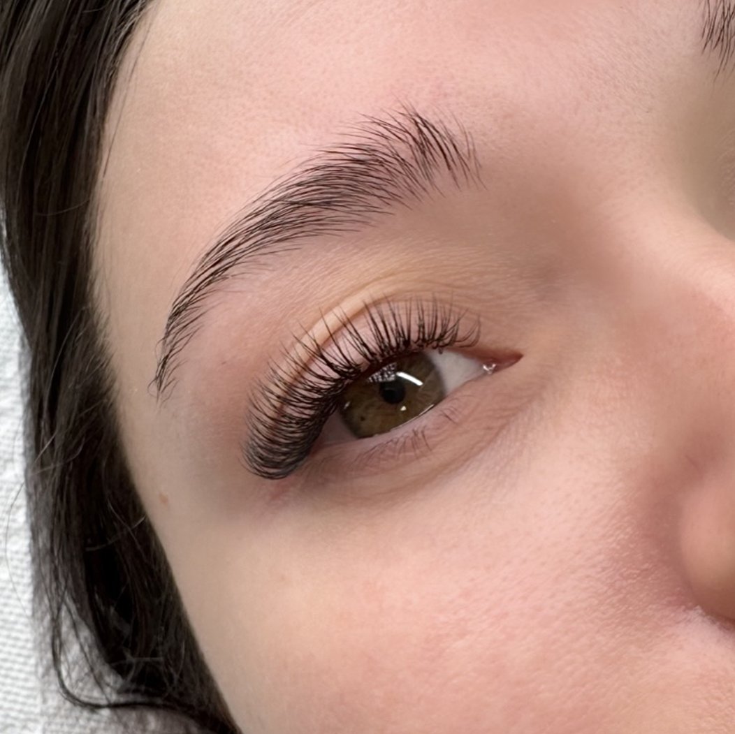 Close-up of a woman's eye showcasing long, curled eyelashes, well-groomed eyebrow, and smooth skin.