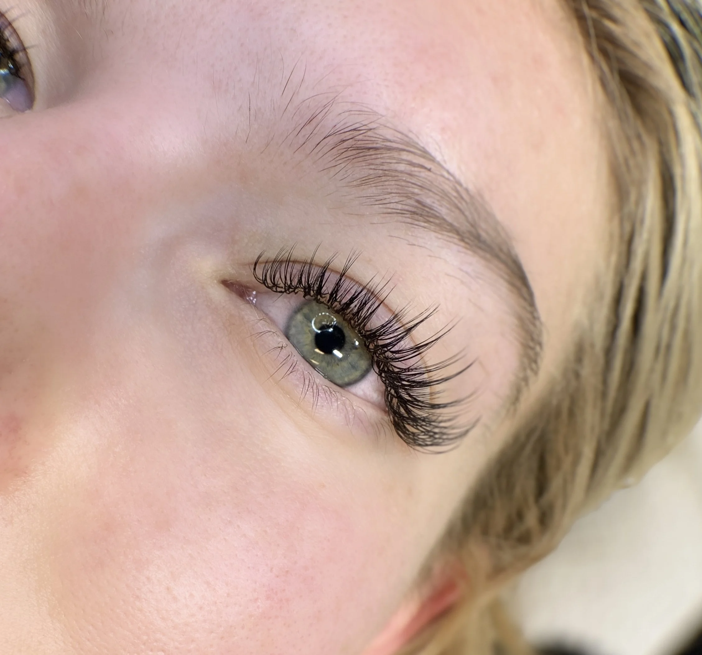 Close-up of a woman's eye with long, curled eyelashes, light skin, and blonde hair.