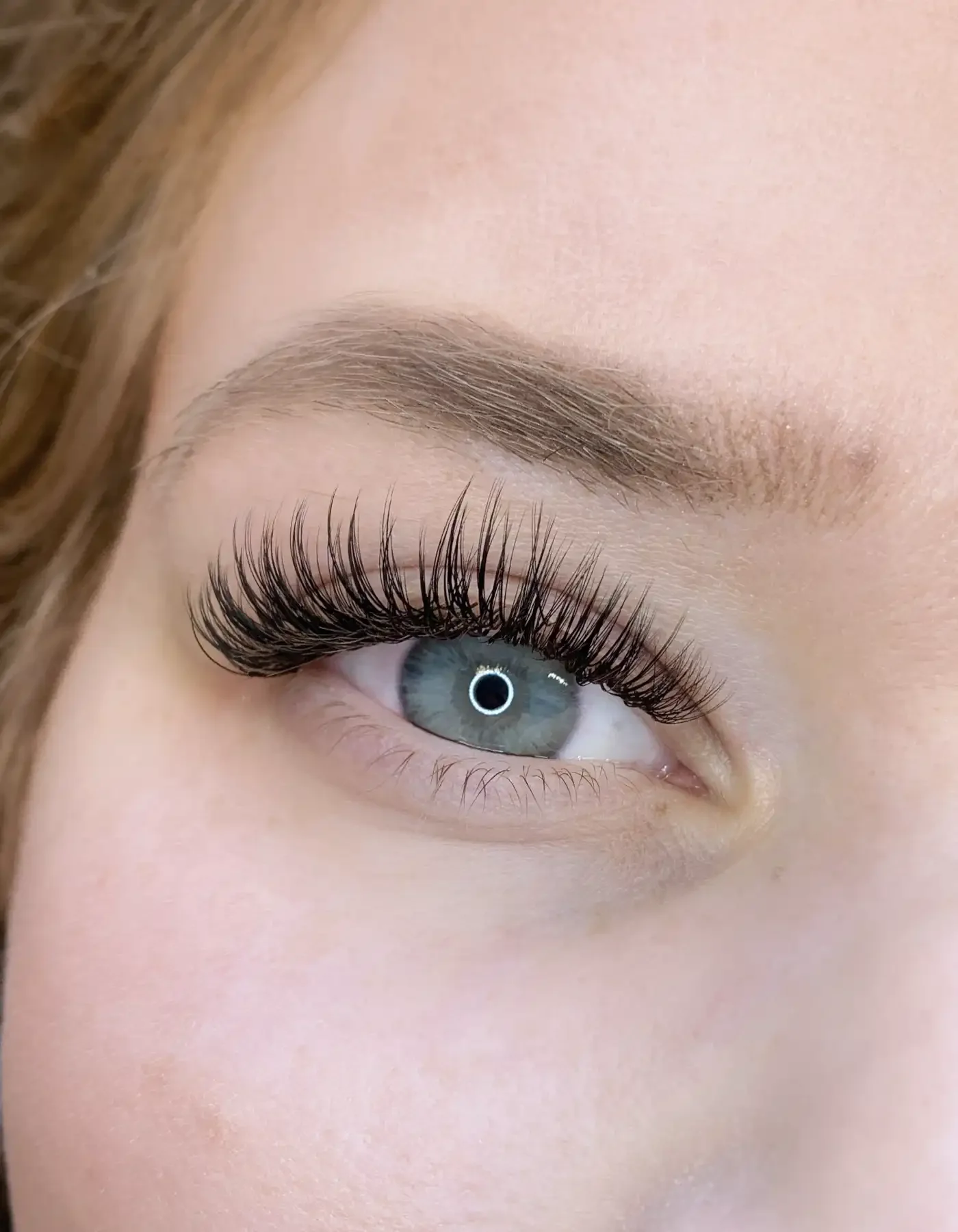 Close-up of a person's eye with long, curled eyelashes, well-groomed eyebrow, and smooth skin.
