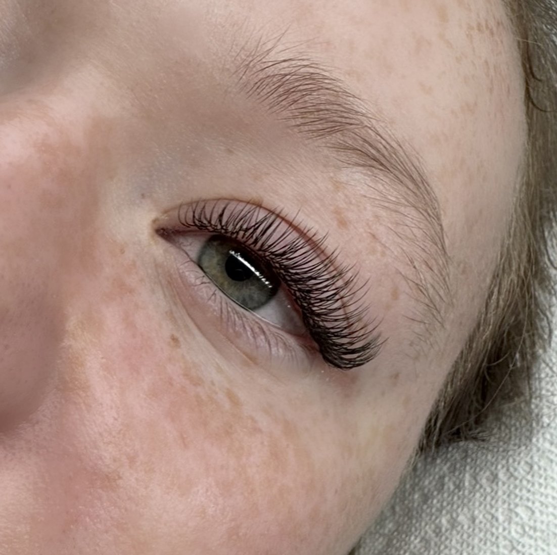 Close-up of a person's eye with long, curled eyelashes, light skin, and visible freckles.
