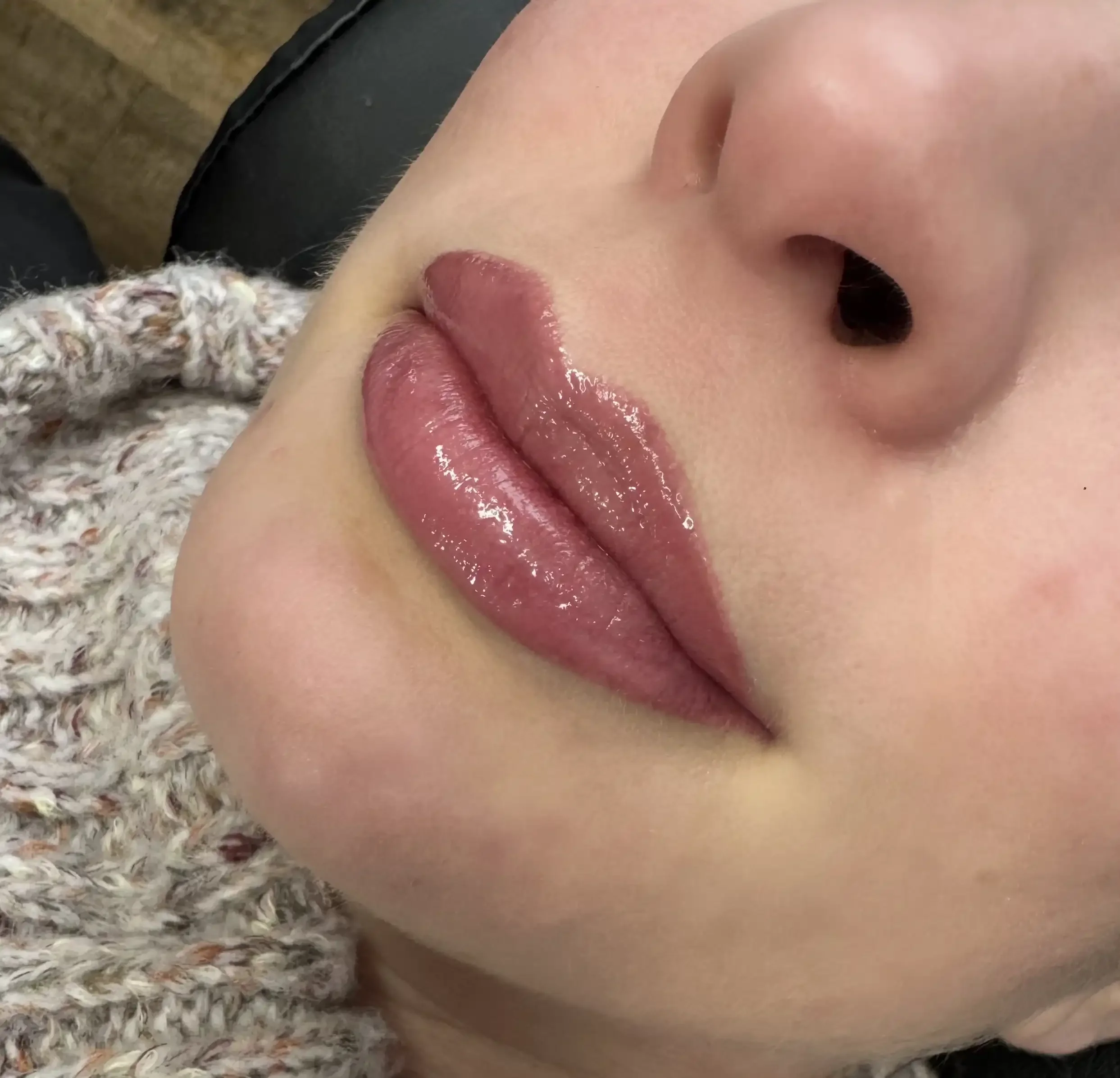 Close-up of a person's face highlighting shiny, pink lips with makeup and a smooth complexion.