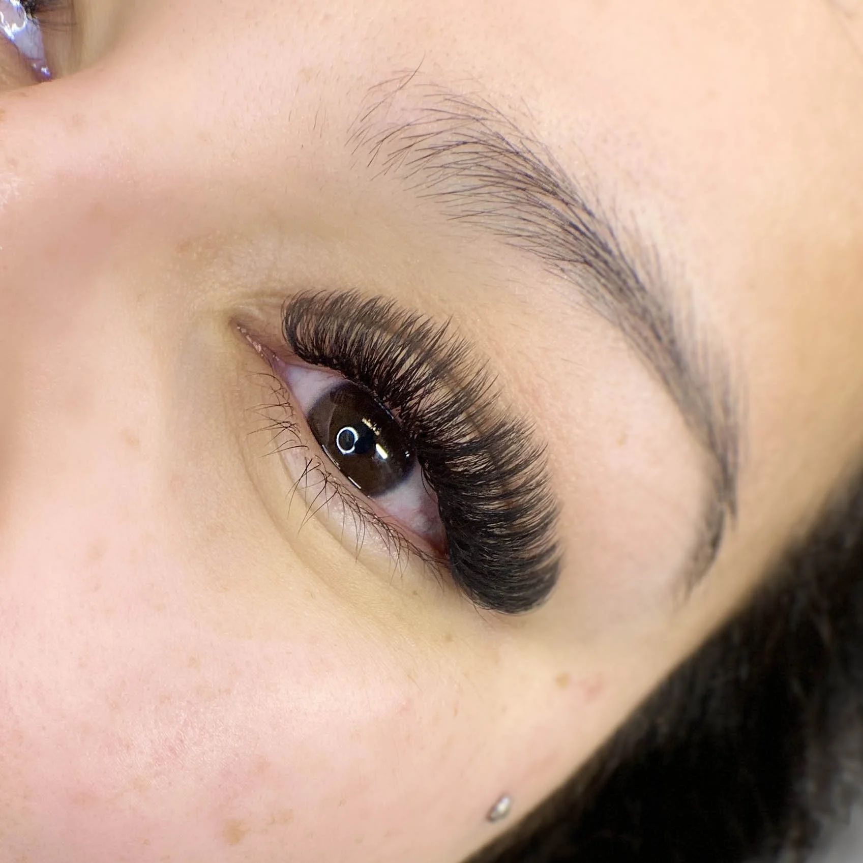 Close-up of an eye with long, thick eyelash extensions, and a visible eyebrow with well-groomed hairs.