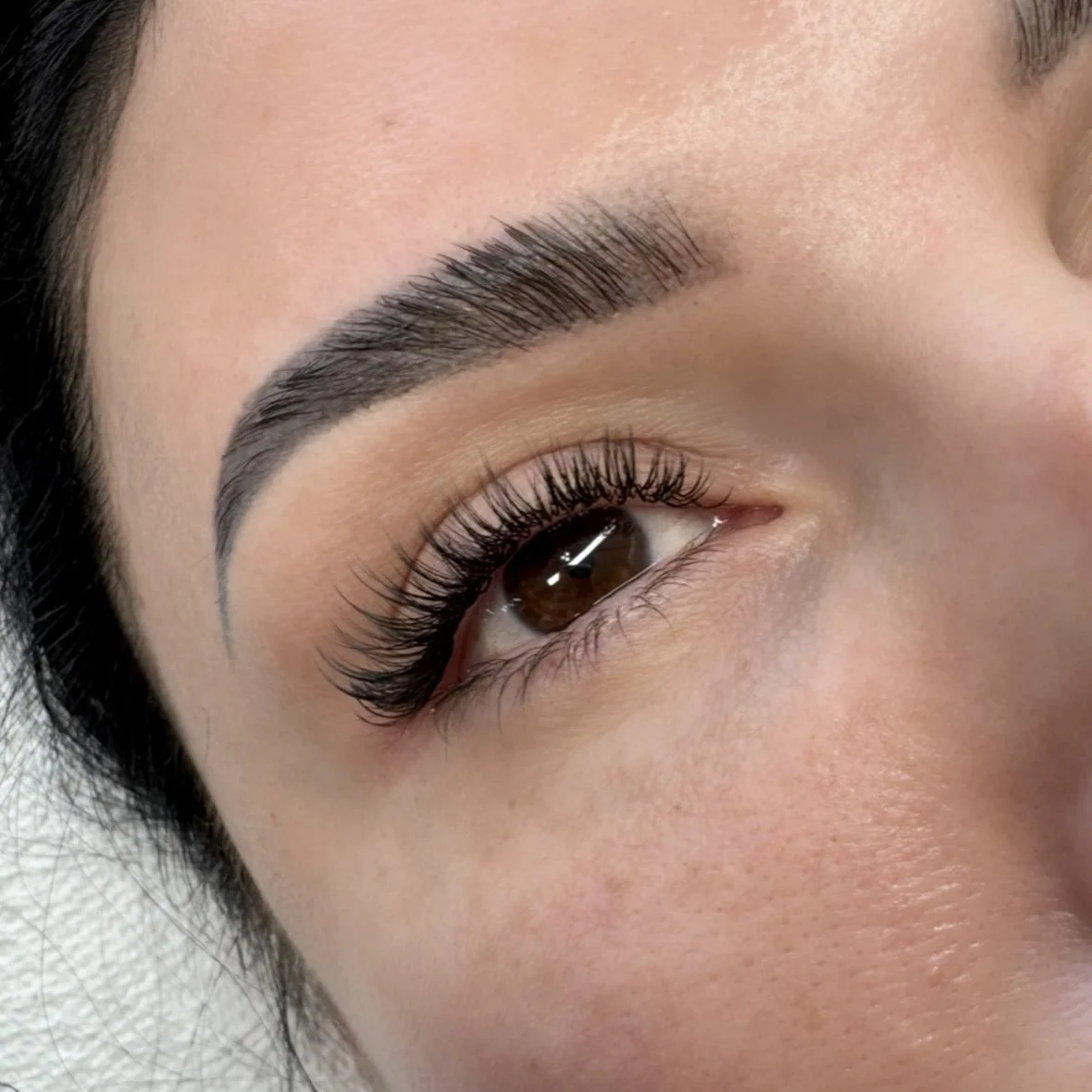 Close-up of a woman's eye with well-defined eyebrow, long eyelashes, and smooth skin.