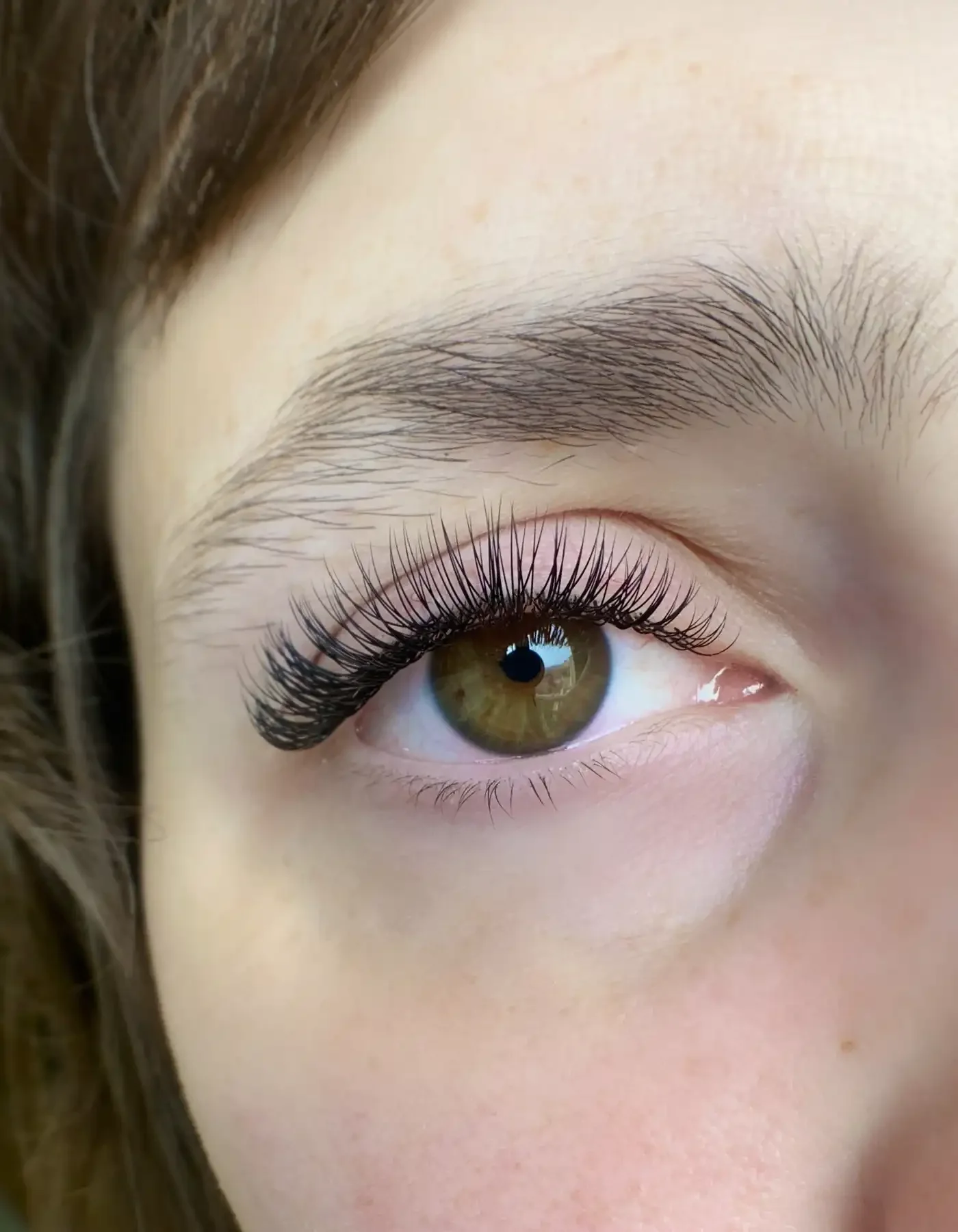 Close-up of a human eye with long eyelashes, green iris, and well-groomed eyebrows.