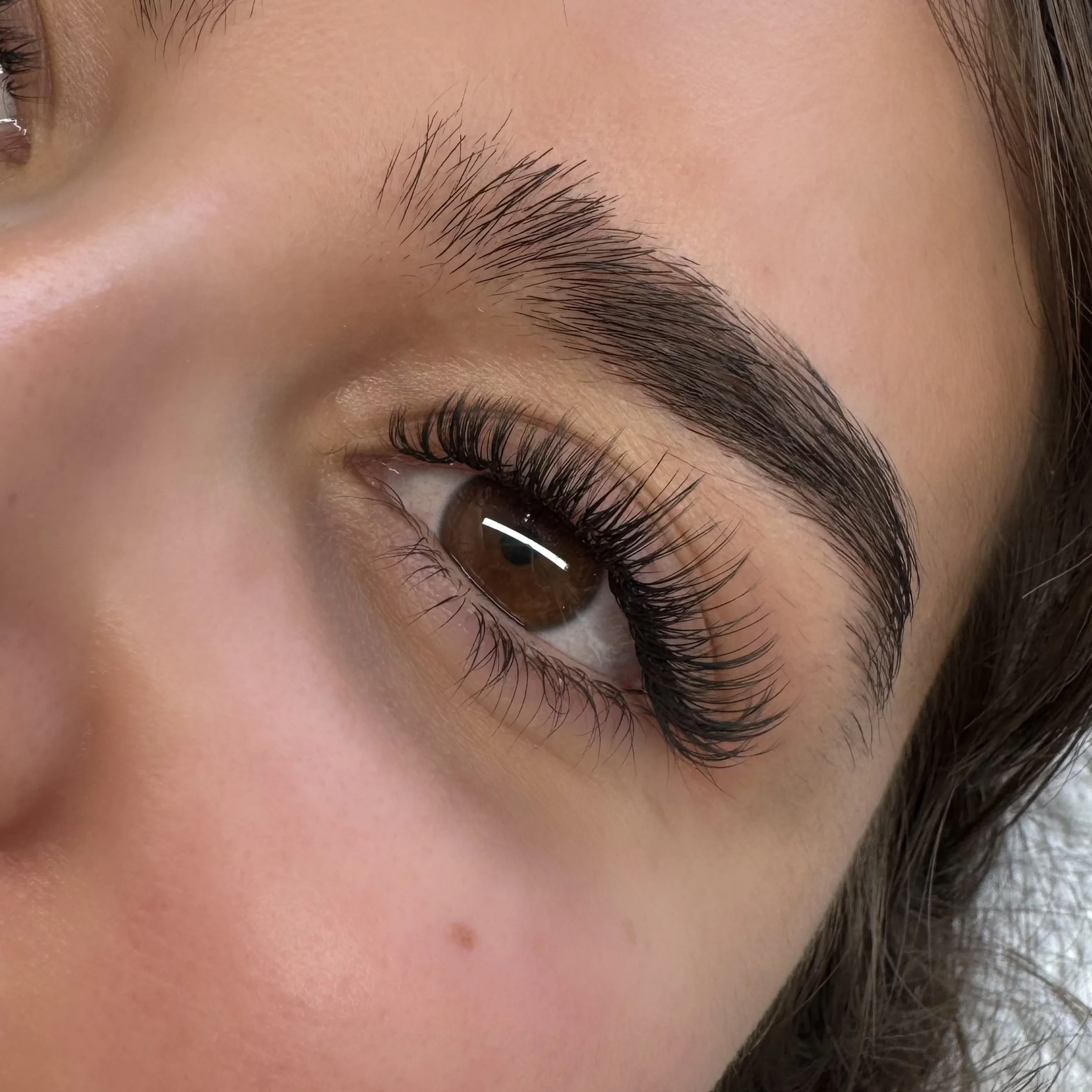 Close-up of a person's brown eye with long, dark, curled eyelashes and well-defined eyebrow.