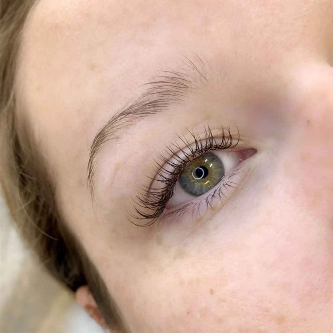 Close-up of a person's eye with long, curled eyelashes and light-colored skin.