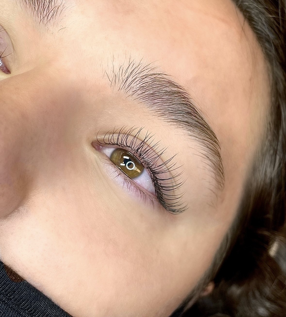 Close-up of a person's face focusing on their eye, eyebrow, and surrounding skin, showing long eyelashes and natural brow hair.