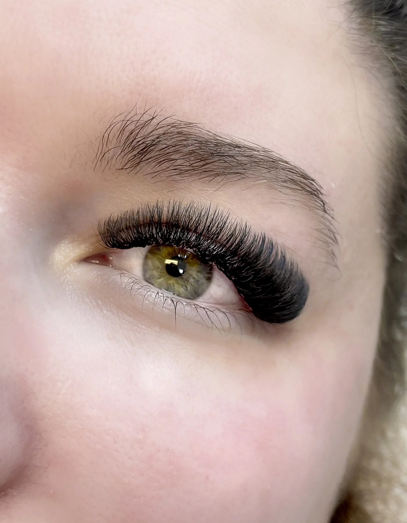 Close-up of a person's eye with green iris, long dark eyelashes, and neatly groomed eyebrow.