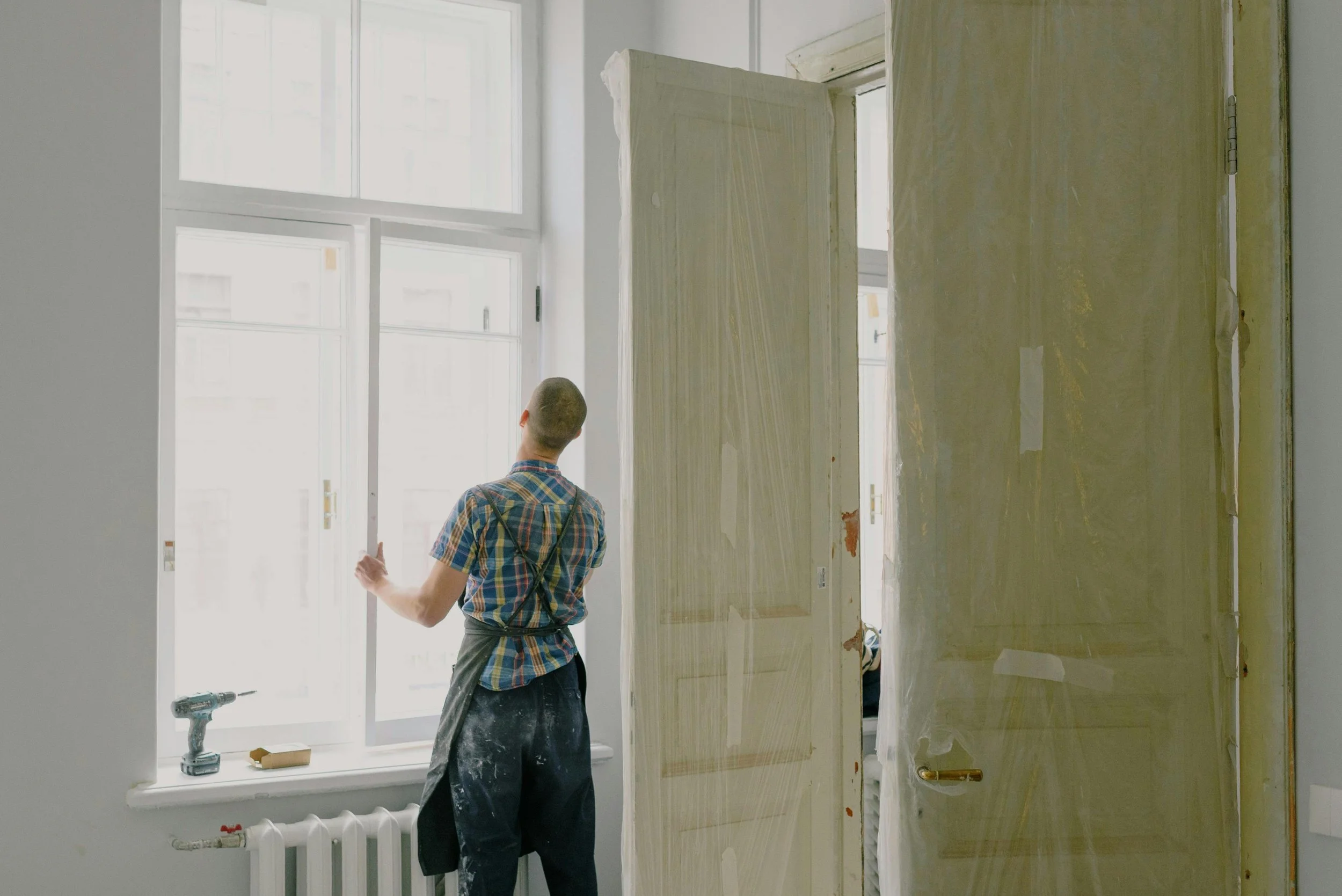 A professional painter standing by a large window, painting a room to an excellent standard during renovation.