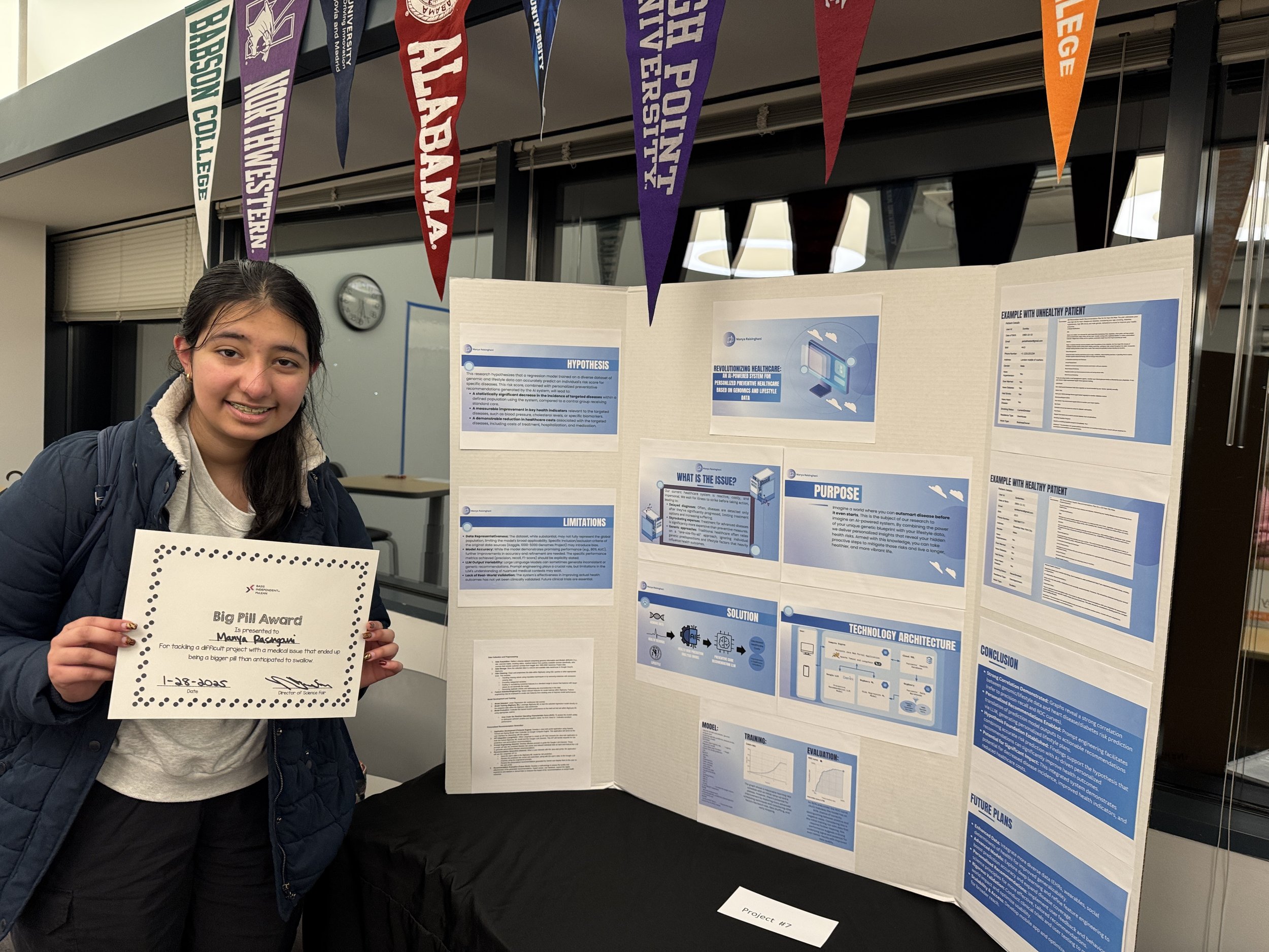 Young woman with dark hair, wearing a navy jacket and light gray hoodie, smiling and holding a certificate that reads 'Big Pill Award' in front of a science project display board at a university event, with purple, red, and orange pennant banners han