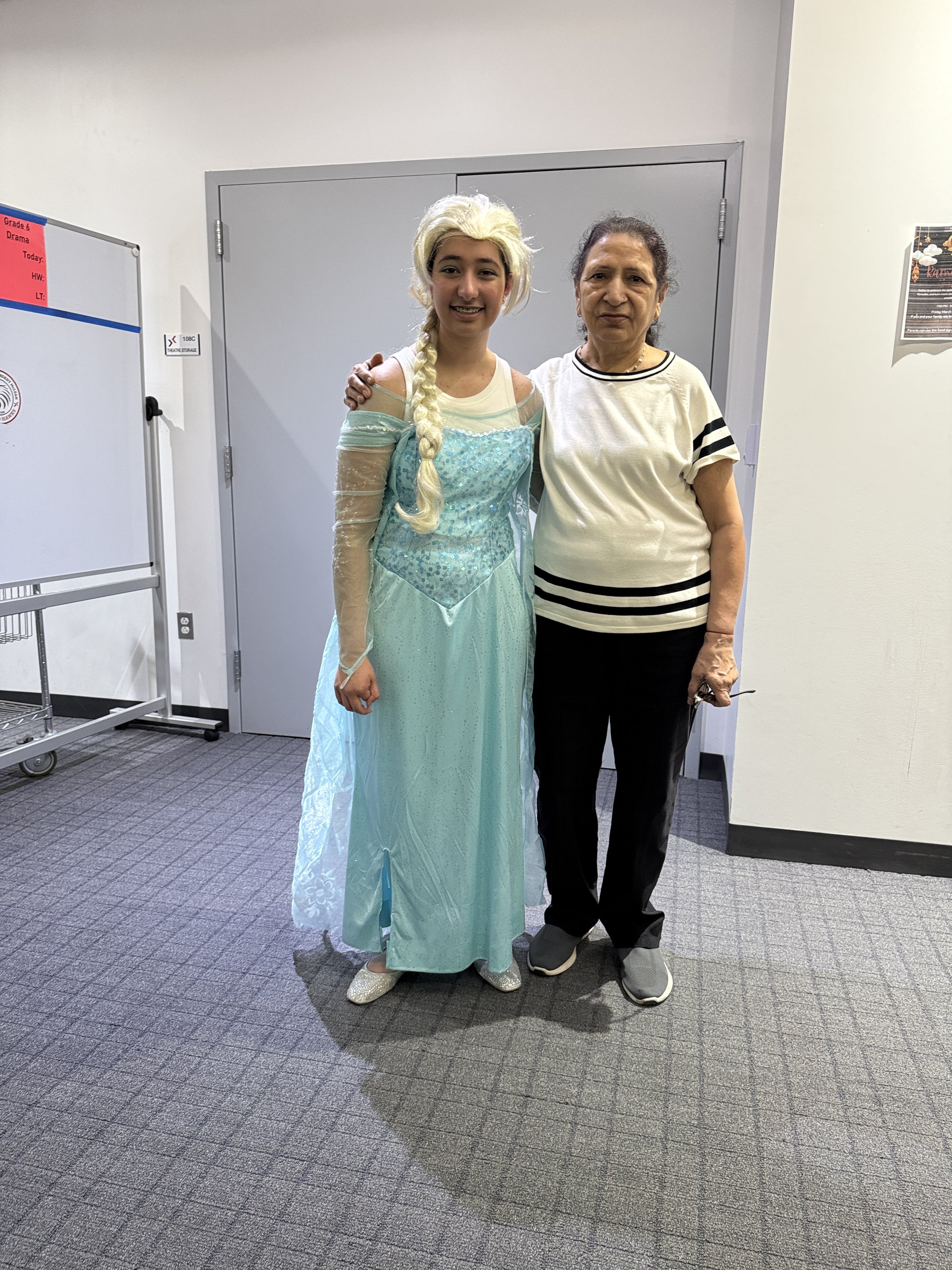 A young woman dressed as Elsa from Frozen standing next to an older woman in casual clothing, both smiling in an indoor setting.