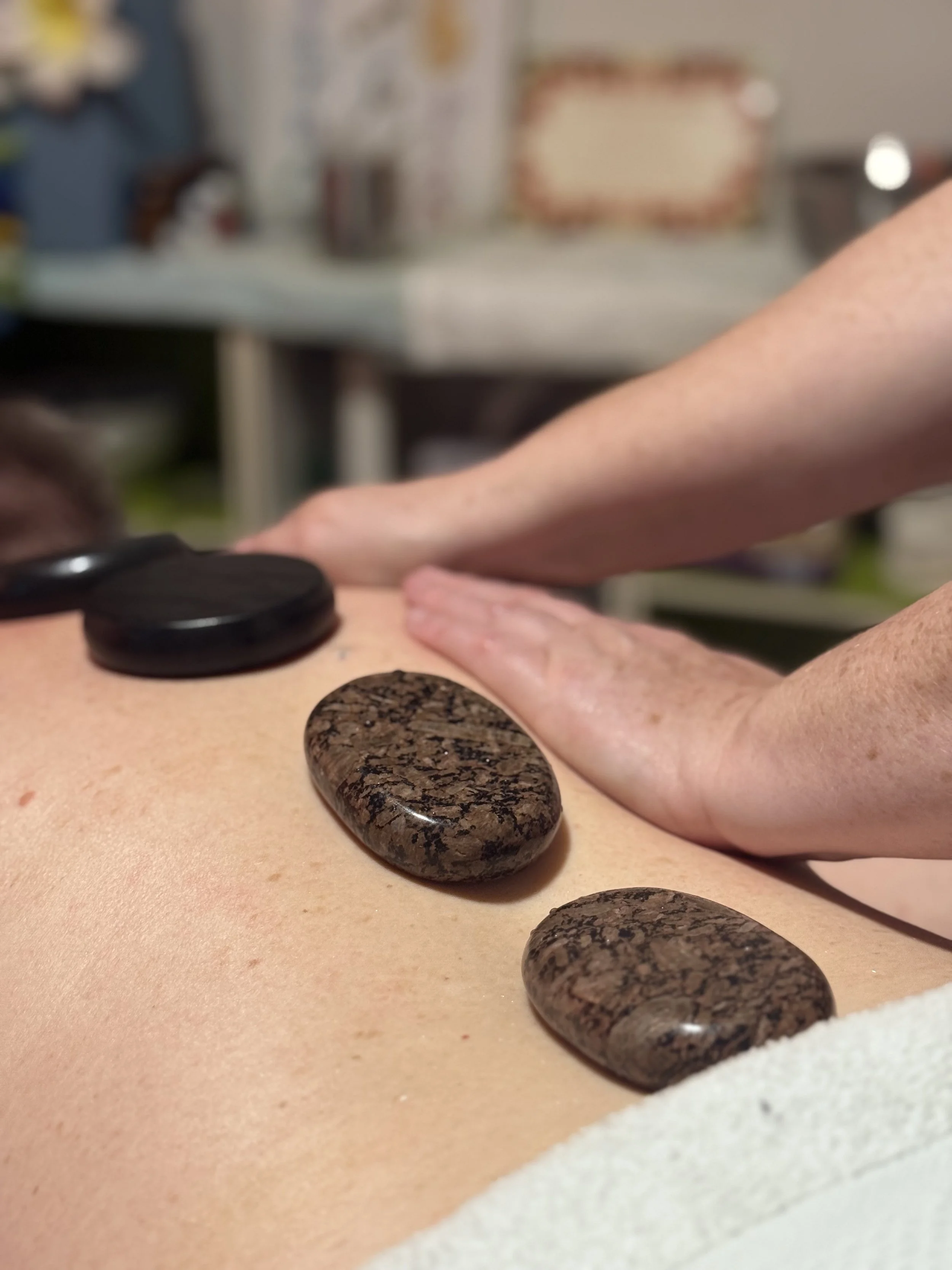 A person receiving a hot stone massage, with several smooth, dark volcanic stones placed along their back.
