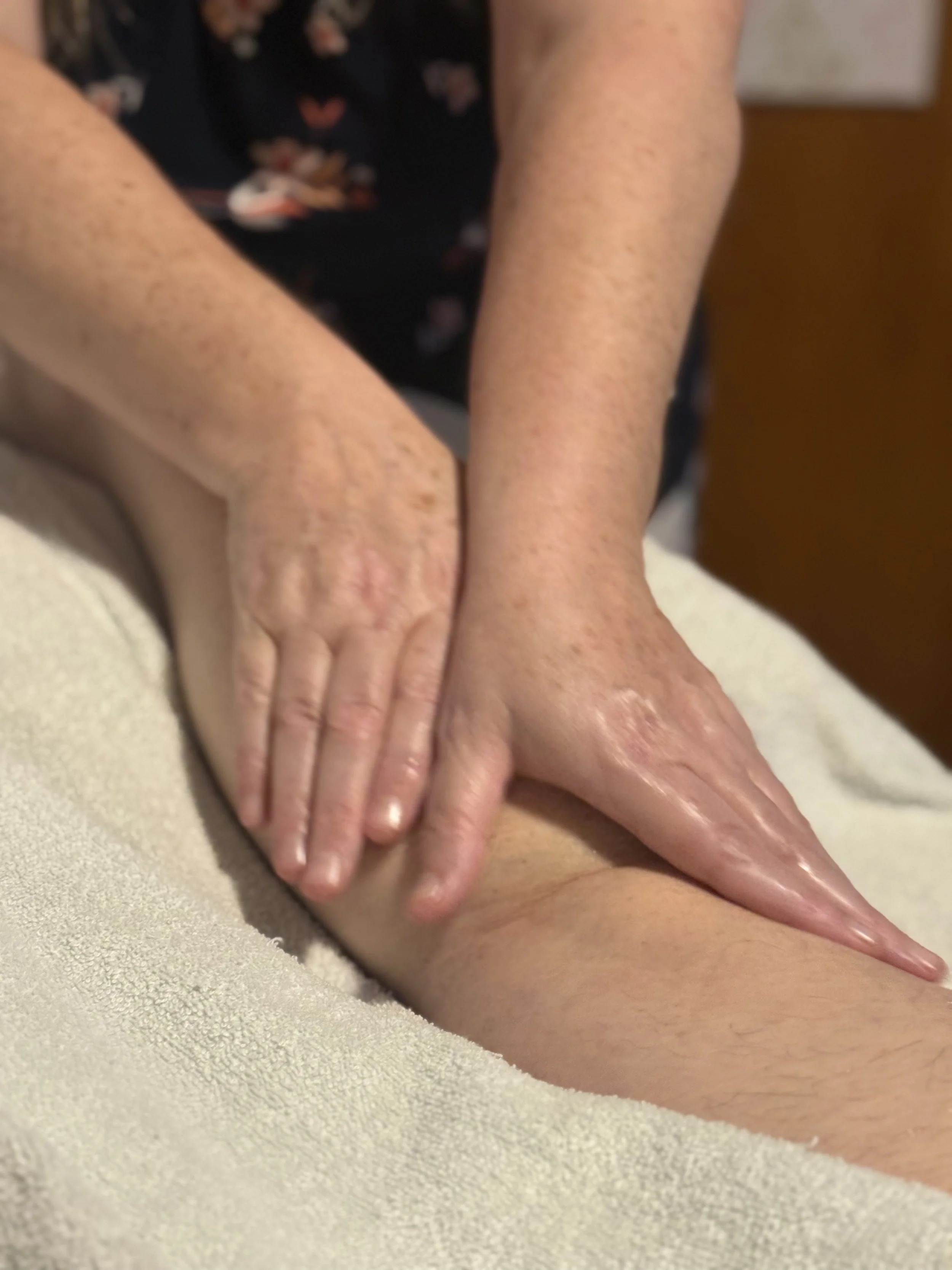 Close-up of a person receiving a massage, with their hand on their thigh and the massage therapist’s hands pressing on their leg.