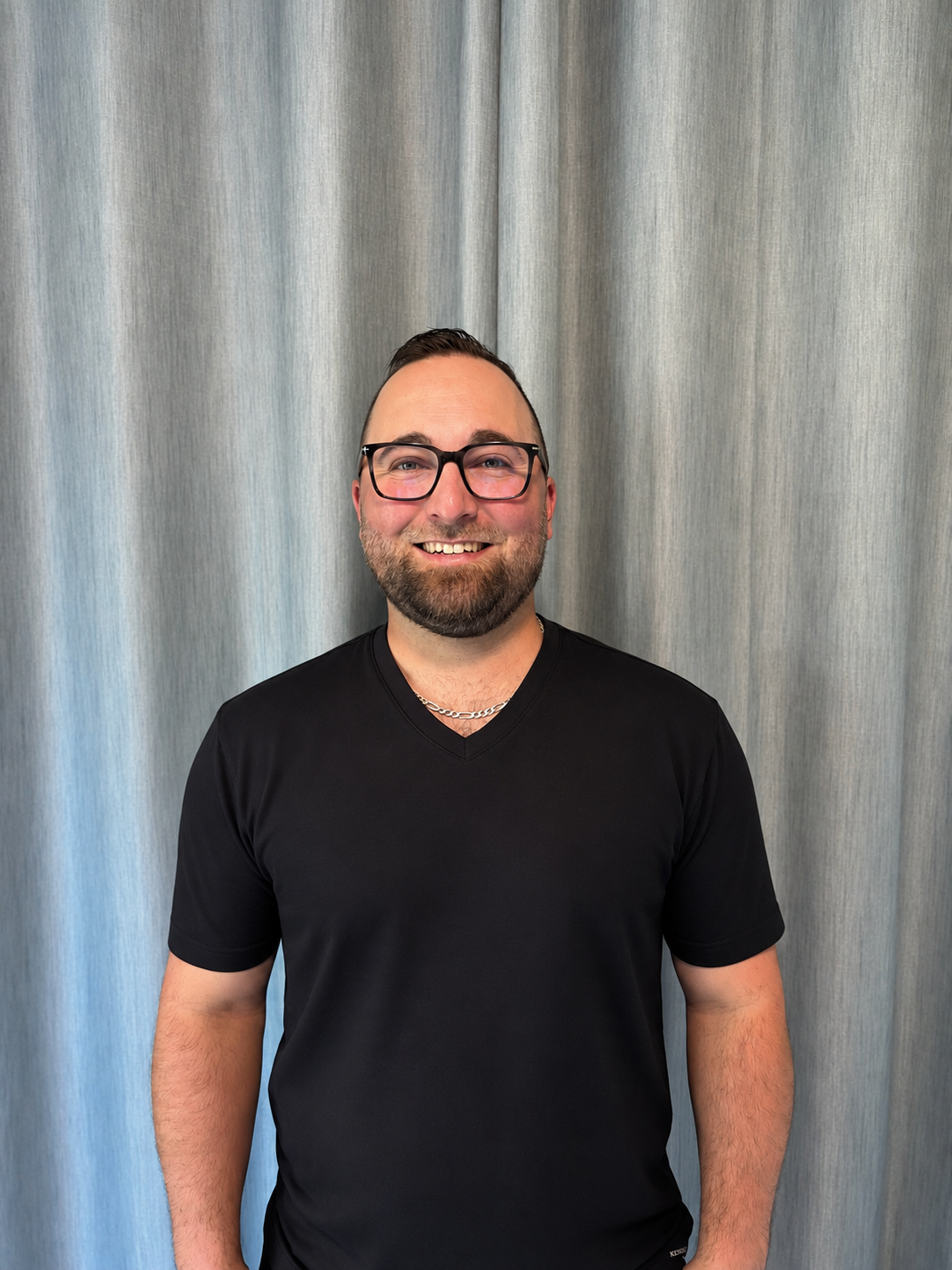 Tyson Popoff in black v neck standing smiling with glasses on