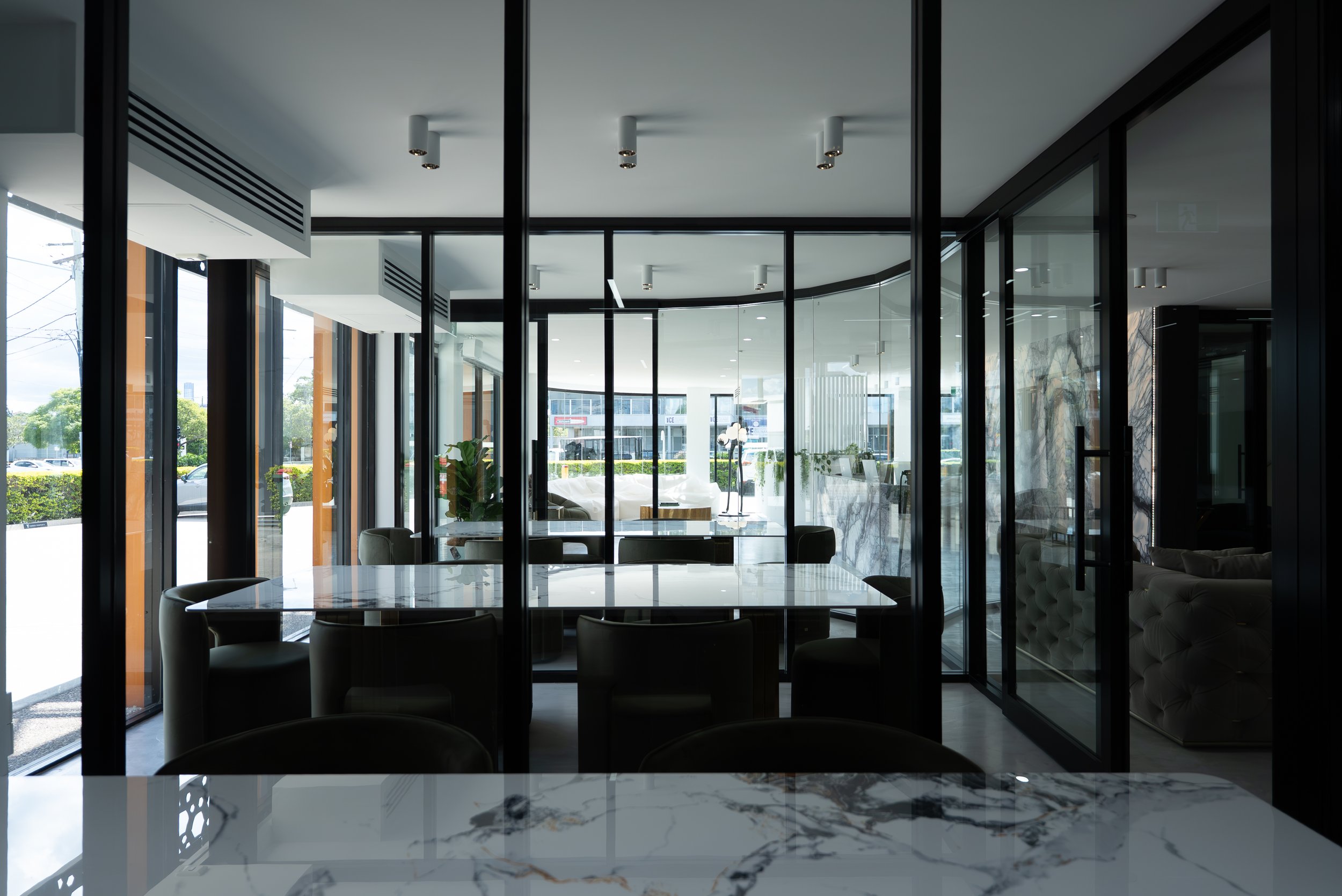 Modern interior of a restaurant or cafe with glass walls, marble tables, and black chairs, with outdoor scenery visible through large windows.