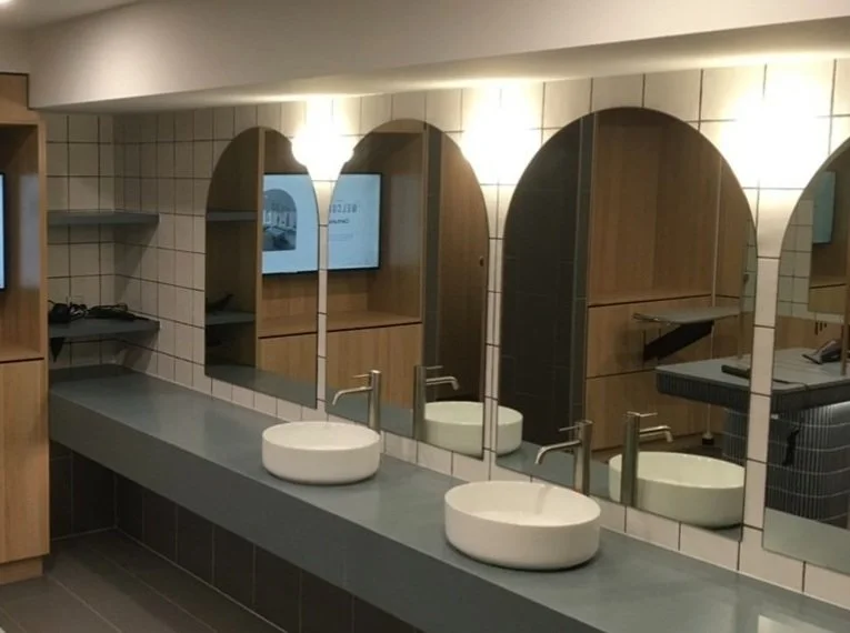 Modern bathroom with three oval sinks, mirrors, and a tiled wall with backlit lighting.