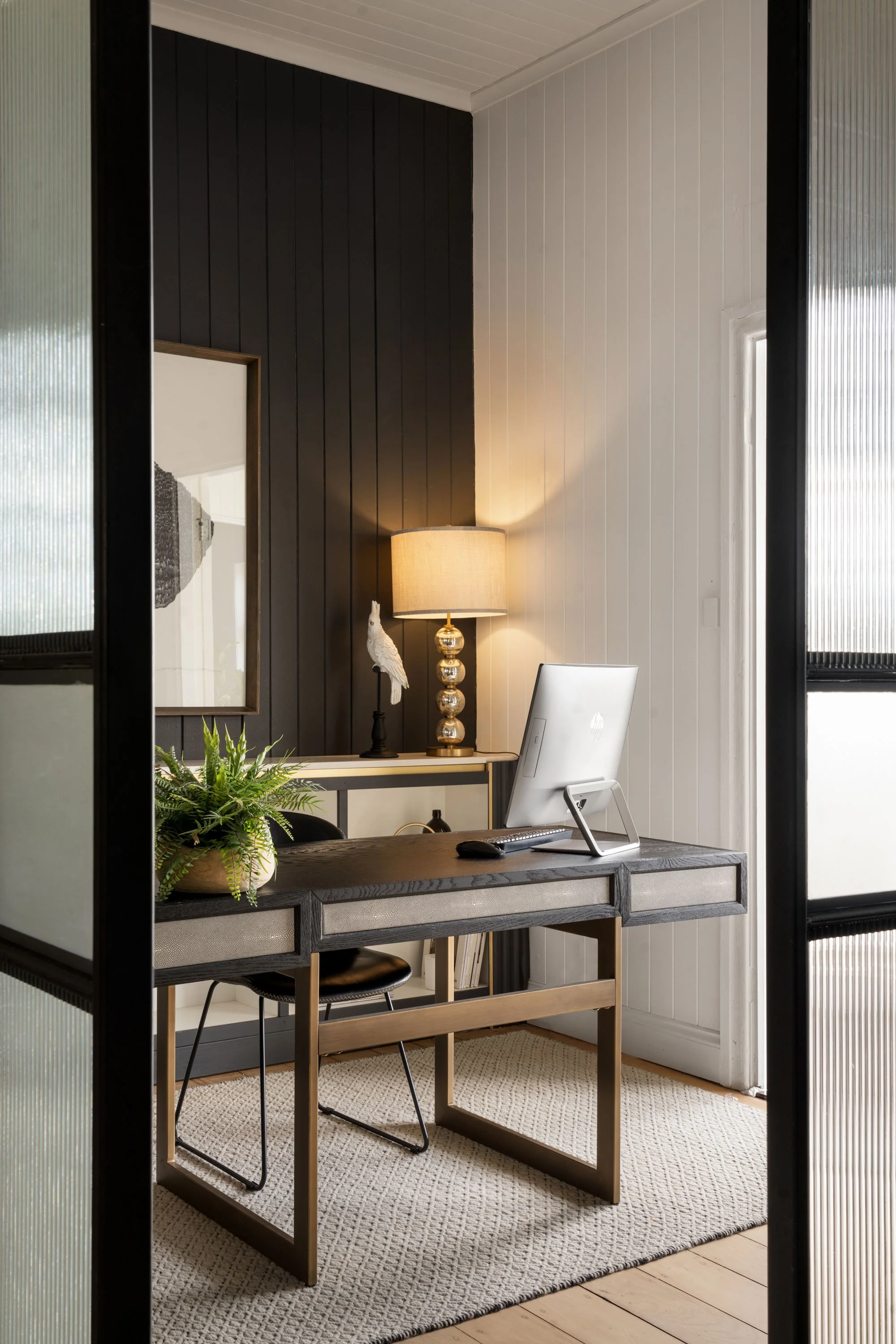 Home office with a black and white wall, desk, computer, lamp, plant, and chair.