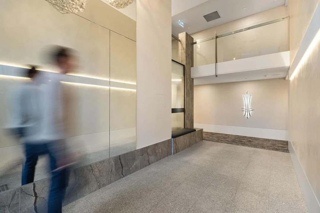 Empty modern lobby with beige walls, marble accents, a sitting bench, and a decorative wall light fixture.