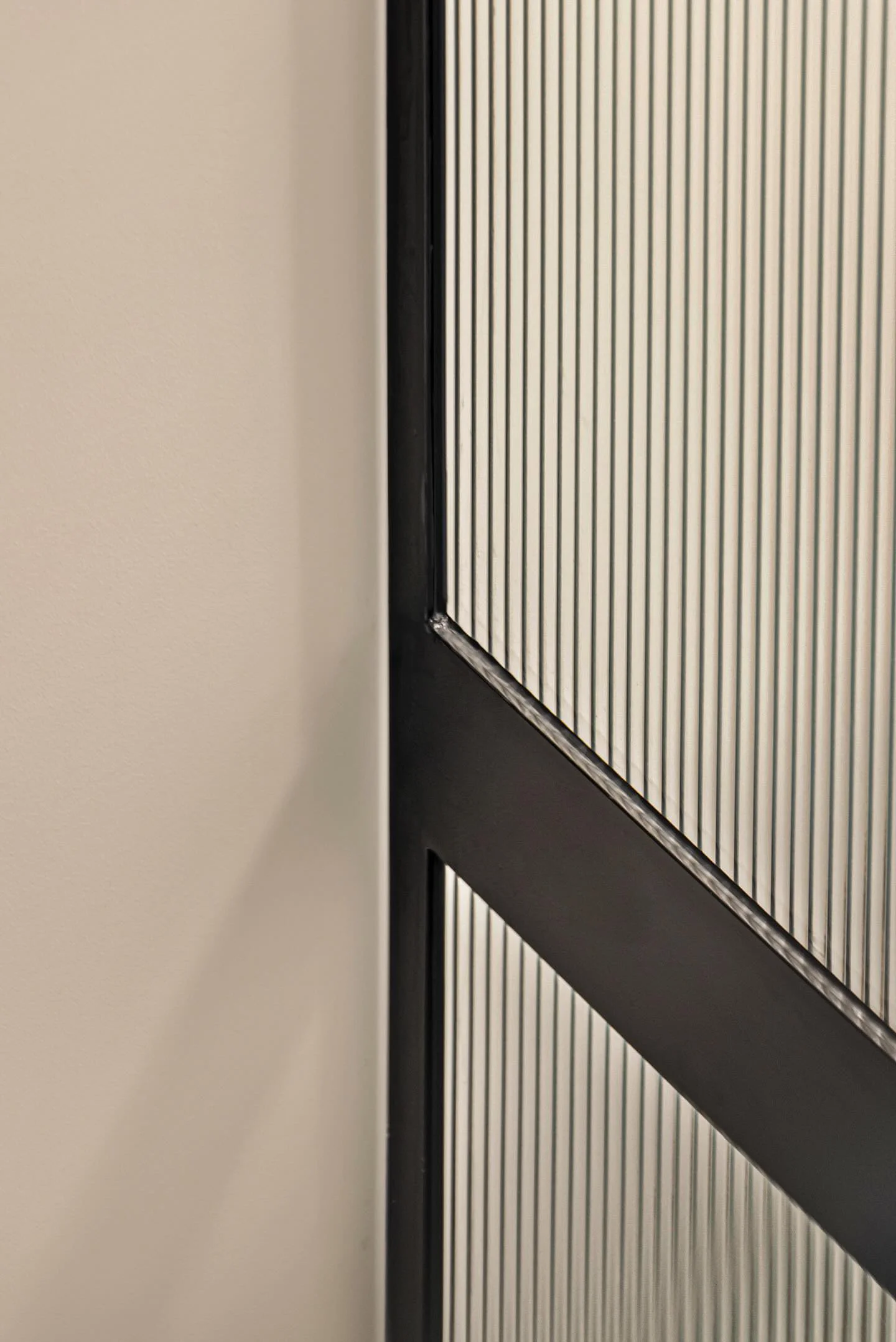Close-up of an elevator door with vertical lines and a black trim, partially visible next to a beige wall.