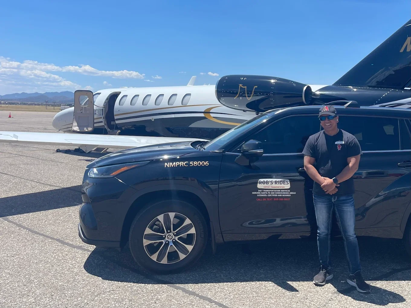 A man standing next to a black vehicle with a logo and contact information, in front of a private jet on an airport tarmac under a clear blue sky.