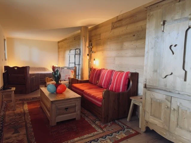 Living room with wooden walls, a red-striped couch, wood coffee table with colorful vases, and a wooden cabinet.
