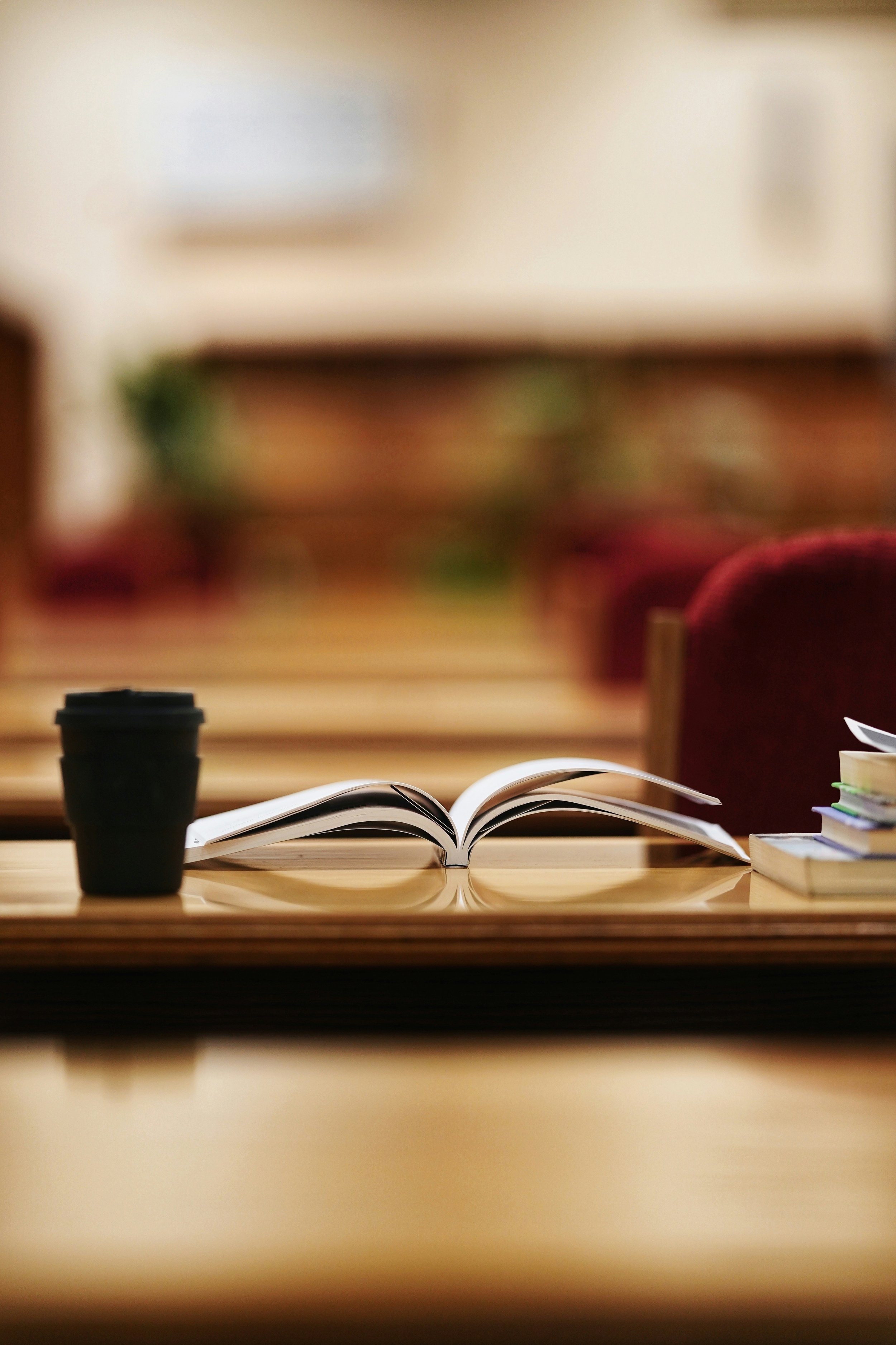 Open book on a wooden table with a black coffee cup and stacks of books, blurred background.