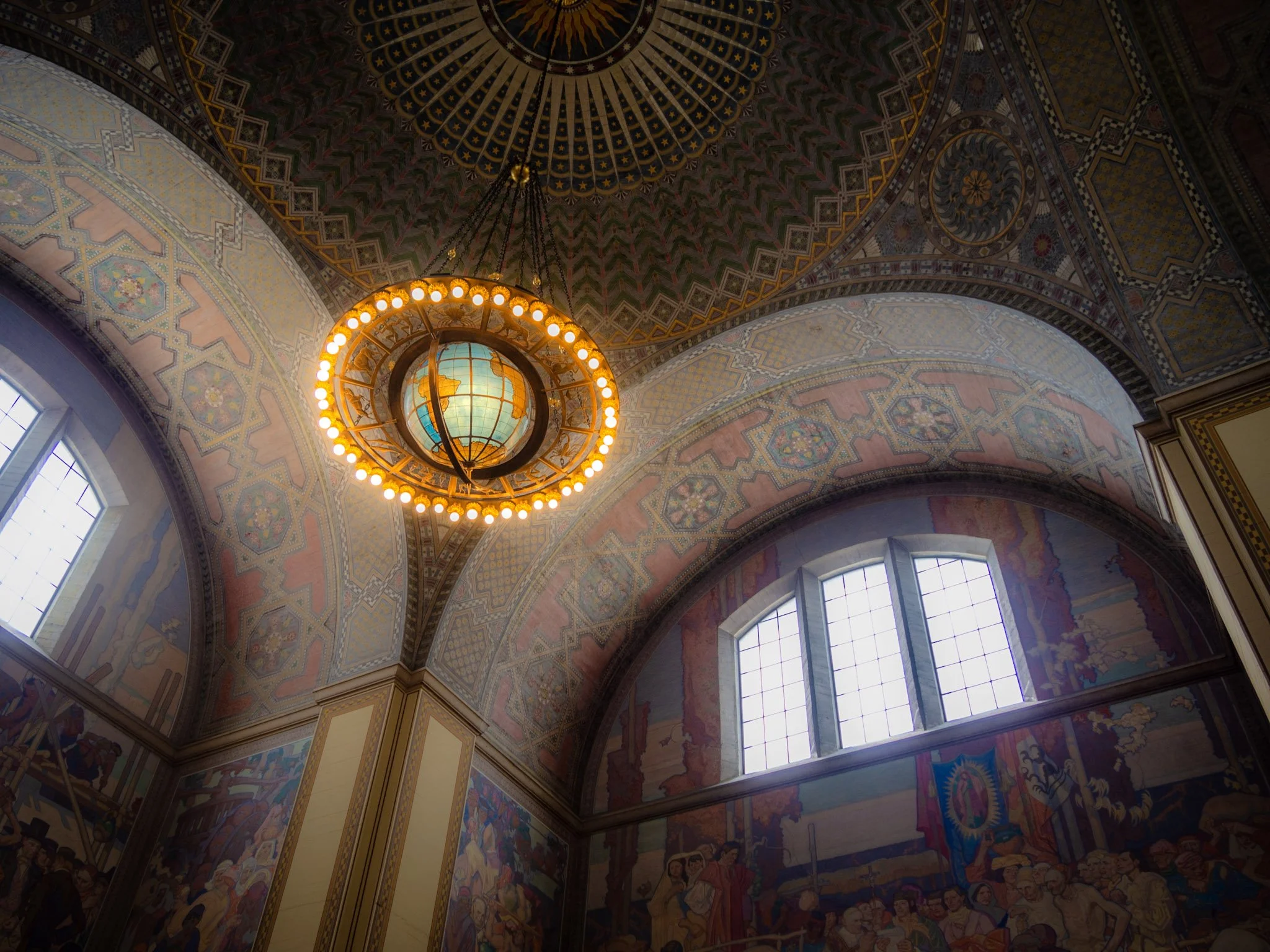 Interior of a grand historic church or cathedral with an ornate painted ceiling, stained glass windows, and a large globe chandelier hanging from the ceiling.