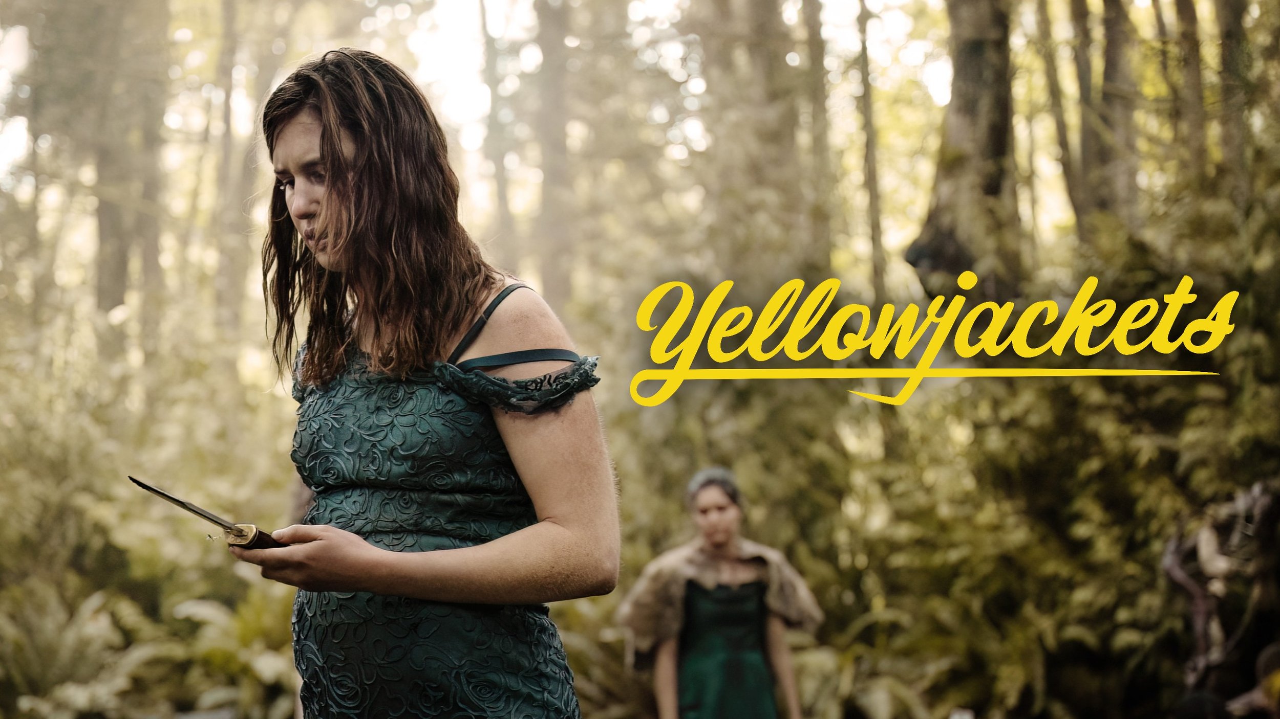 A woman with dark wavy hair wearing a dark green dress standing in a forest, holding a small book, with two women in the background and yellow text that reads 'Yellowjackets'.