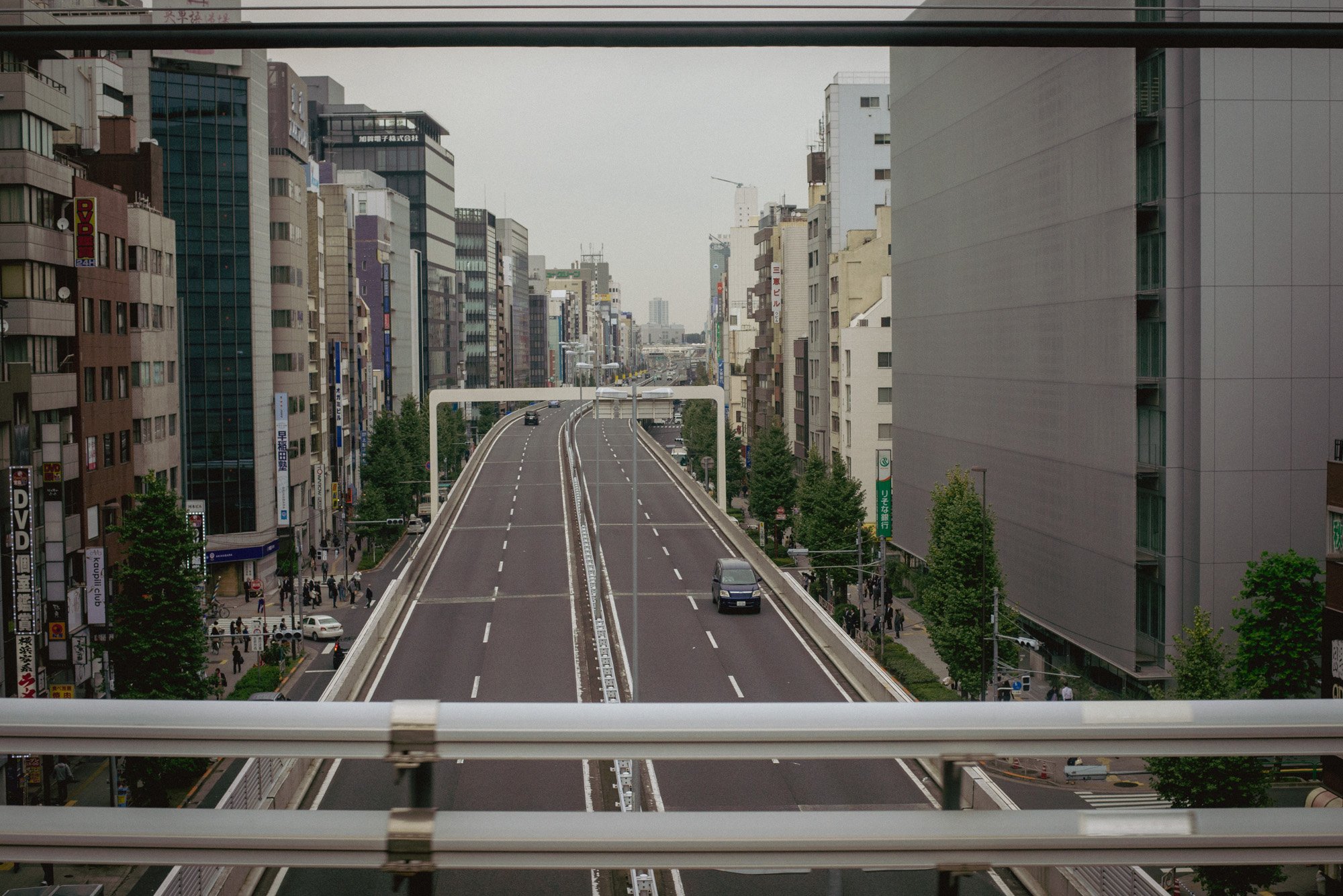 A view of a highway between buildings in Tokyo, seen from a train car.