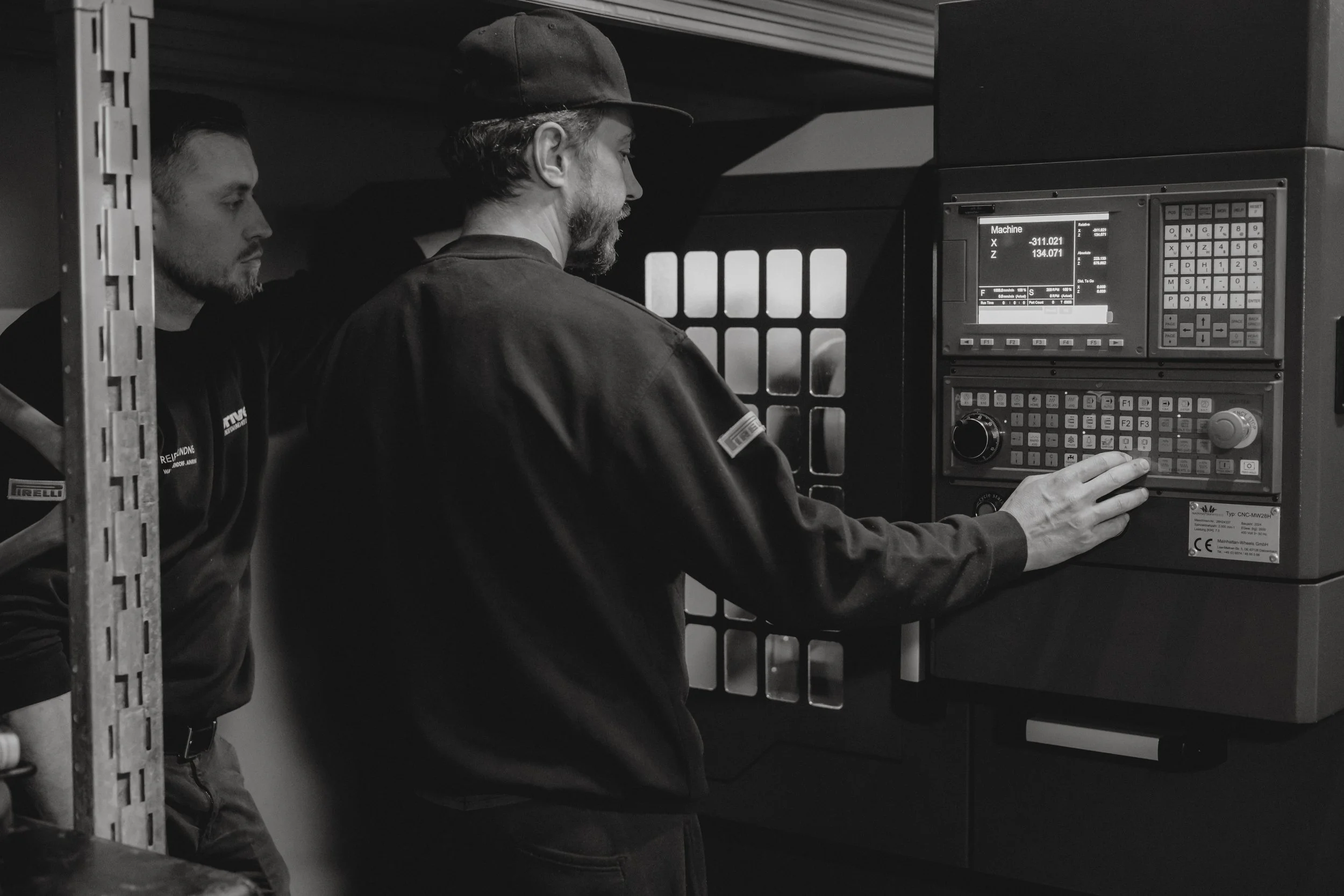 Zwei Männer bedienen eine CNC-Maschine in einer Werkstatt, schwarz-weiß Fotografie.