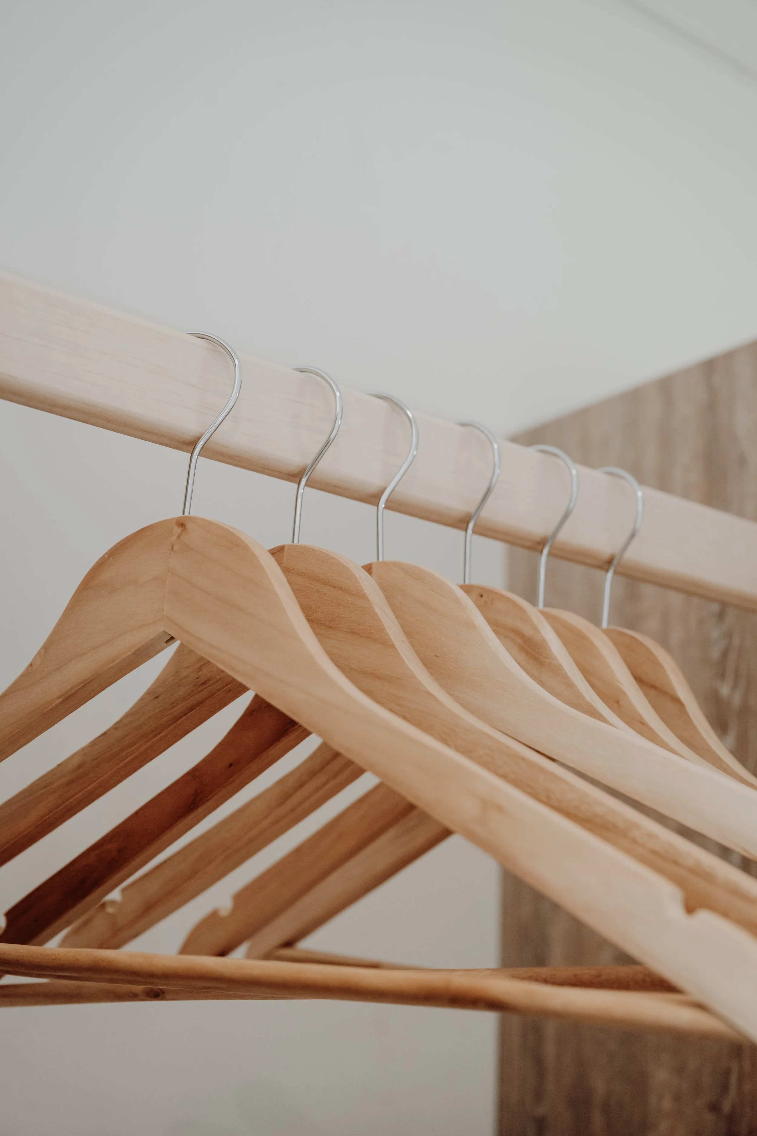 Several wooden hangers hanging on a metal rod inside a closet.