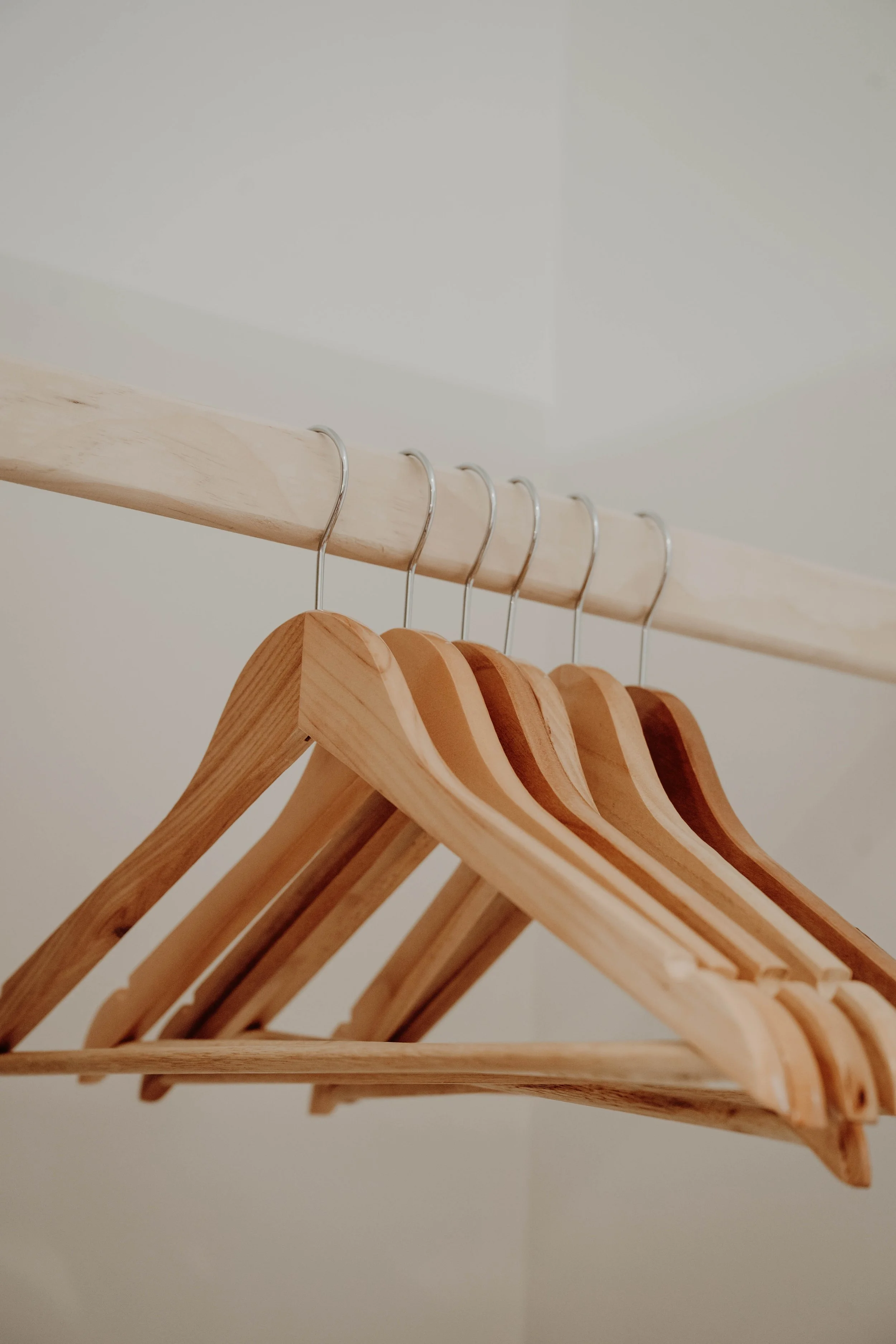 A close-up of wooden and plastic hangers hanging on a light wooden rod in a closet.