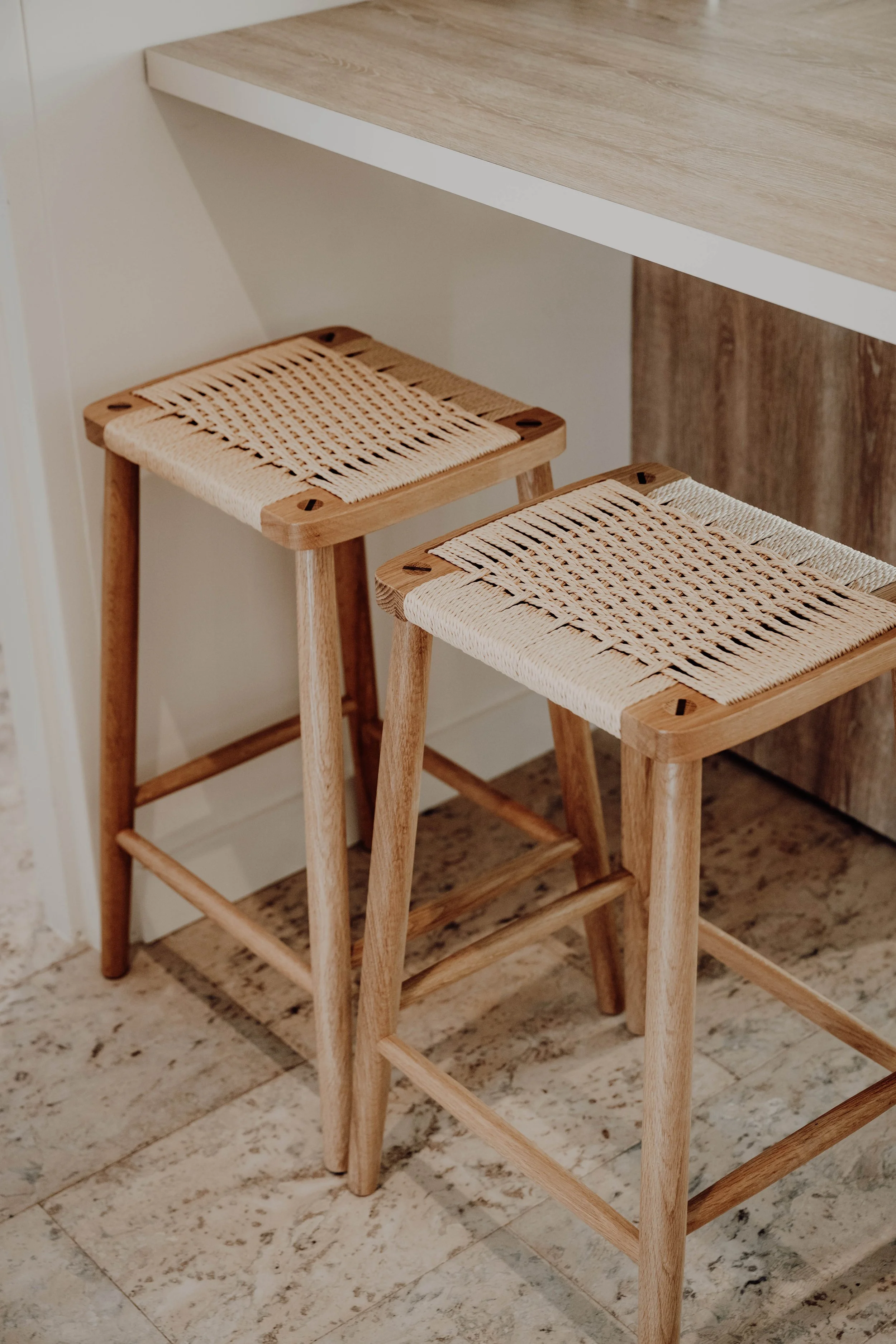 Two wooden bar stools with woven beige seats under a wooden countertop in a modern kitchen.