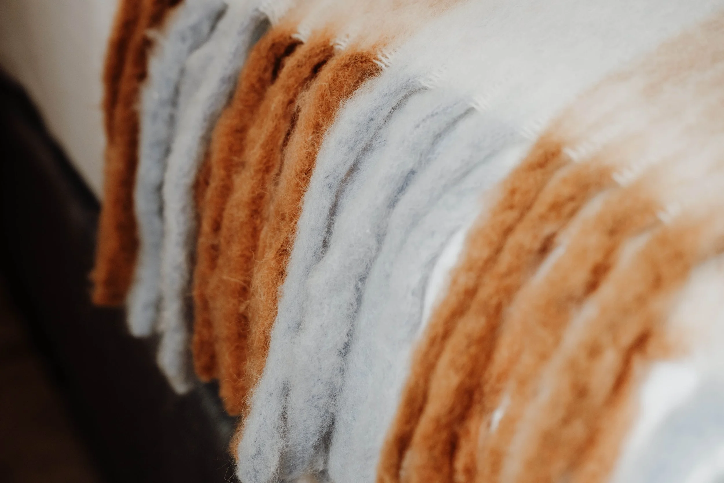 Close-up of various colorful felted wool fabric strips in white, orange, and brown hues.