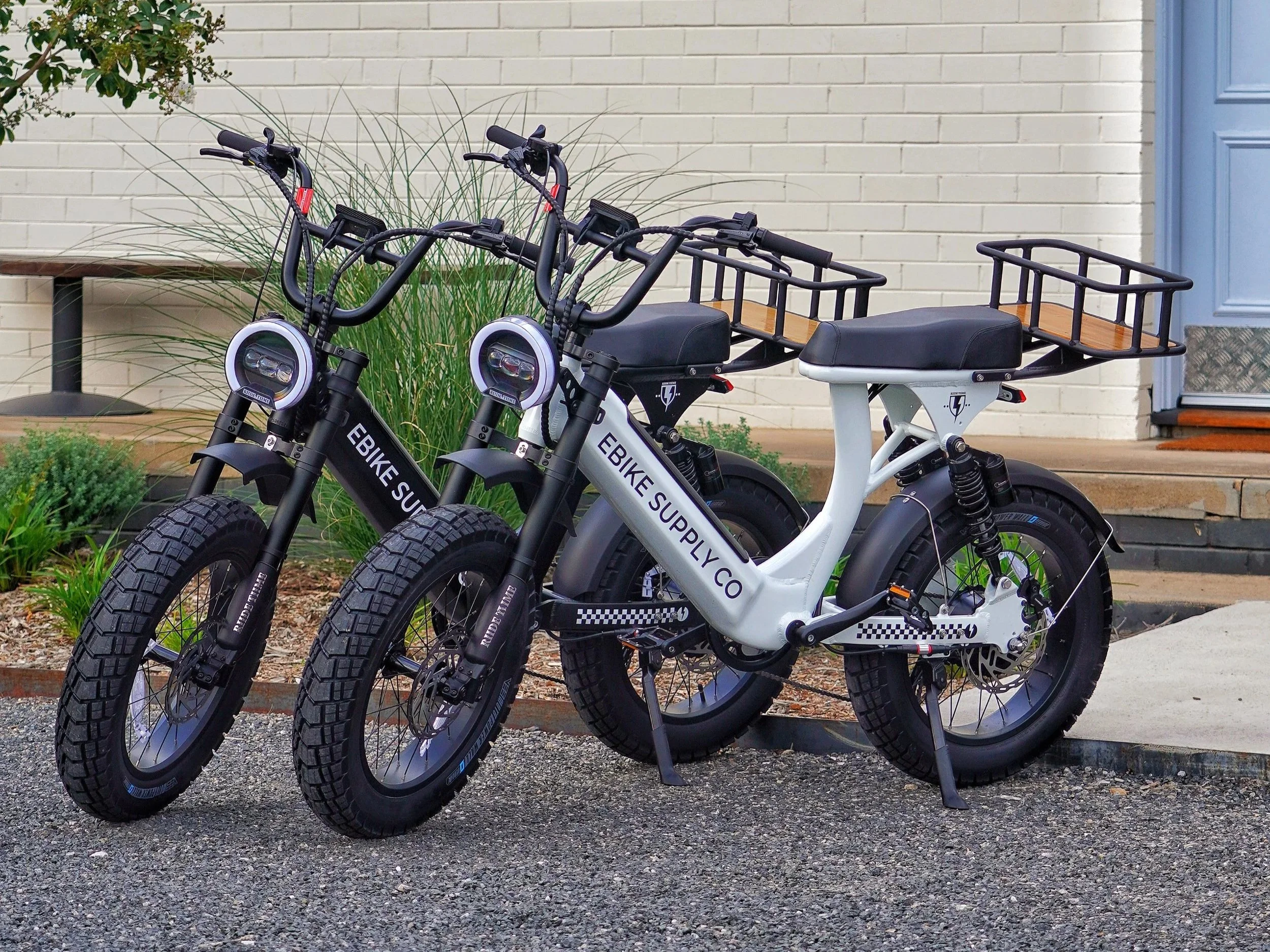 Hot air balloon with yellow and black checkered pattern flying over grassy field at sunrise, with visible flame from the burner and trees in the background.