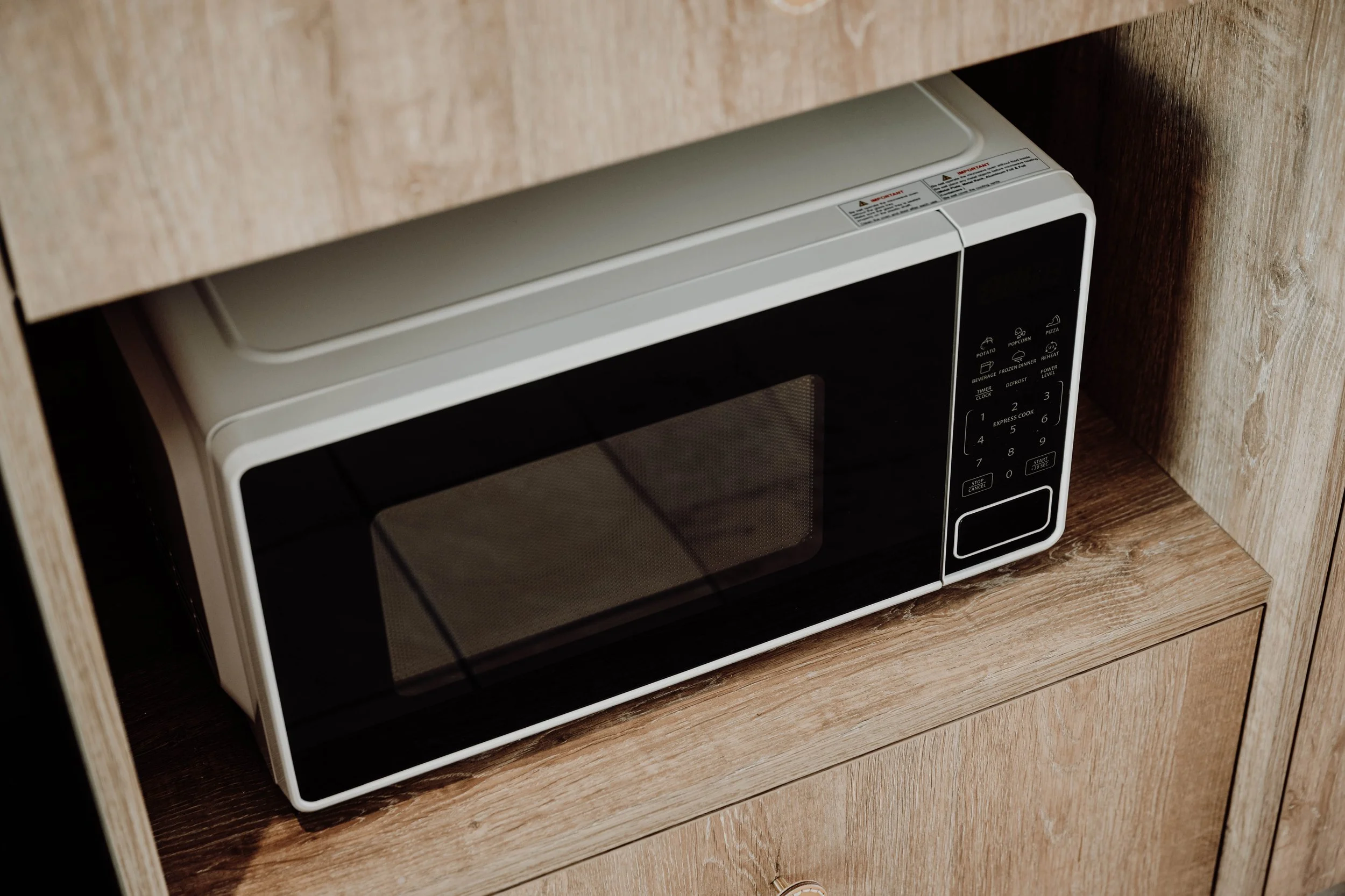 A microwave oven on a wooden kitchen counter with a wood-paneled wall behind it.