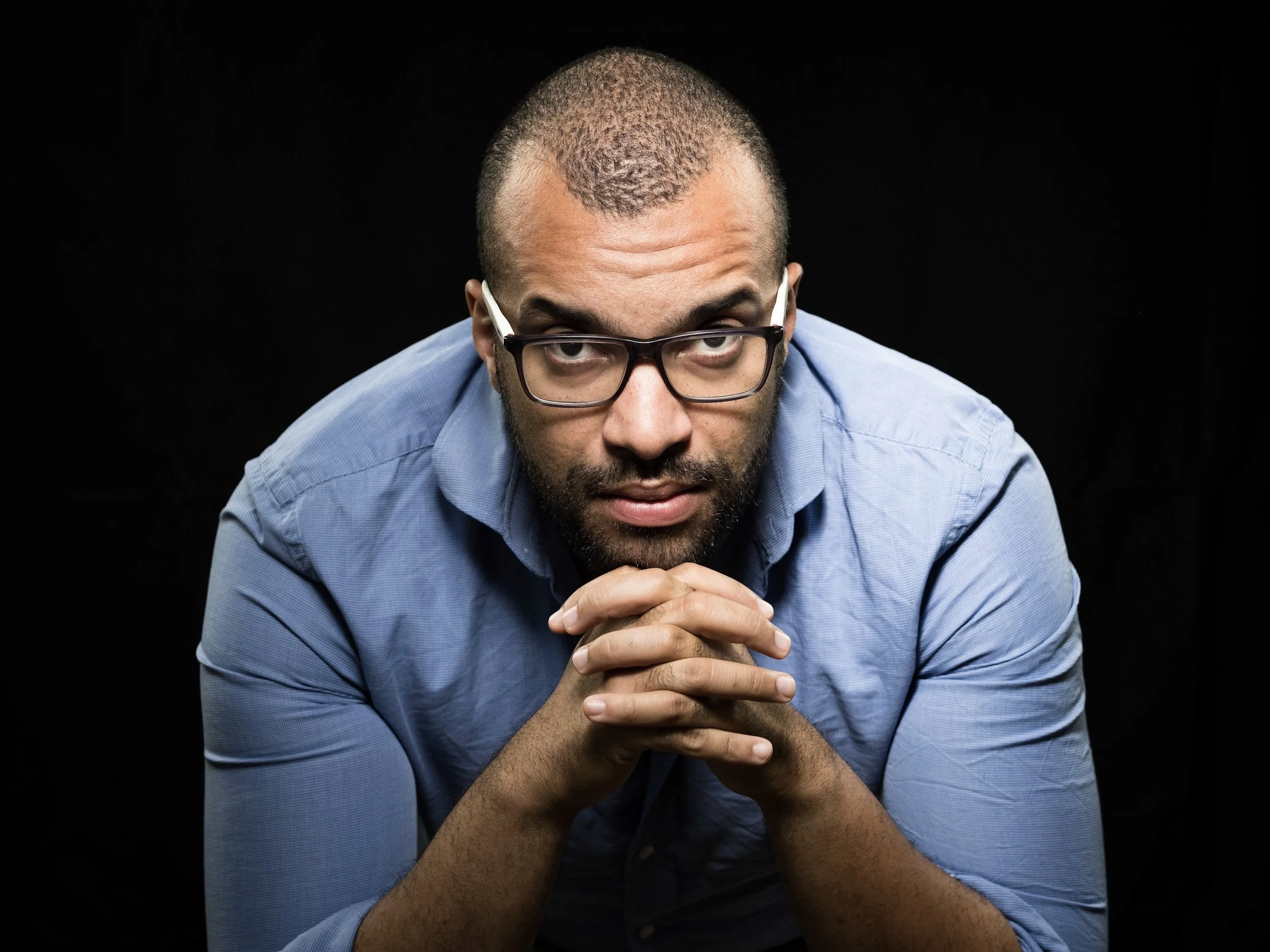 Thomas Stimmel trägt ein blaues Hemd, blickt direkt in die Kamera, hat den Kopf gesenkt und die Hände verschränkt.