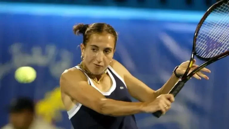 A woman playing tennis on a court, preparing to hit a yellow tennis ball with a racket.