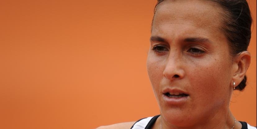 Close-up of a woman with brown hair pulled back, wearing a black and white athletic top, against an orange background.