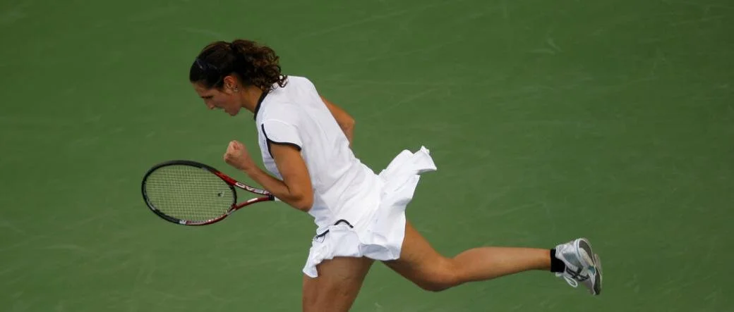 Female tennis player in white dress celebrating on a tennis court.
