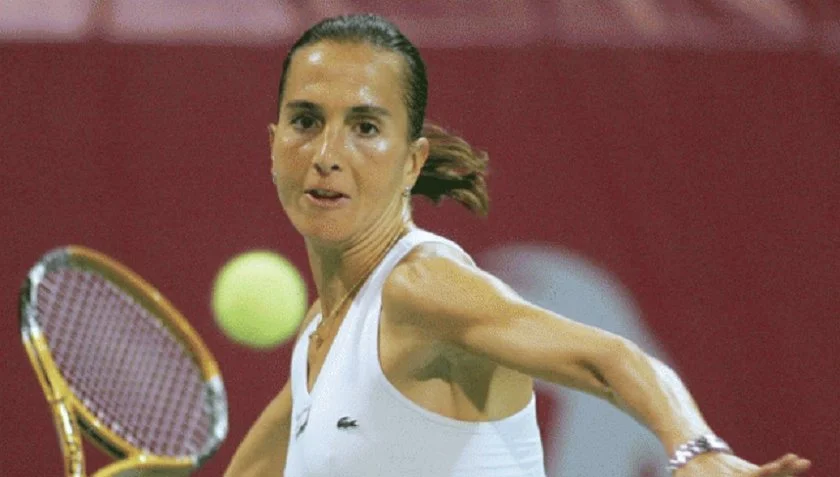 A female tennis player in a white tank top hitting a tennis ball with a racket during a match.