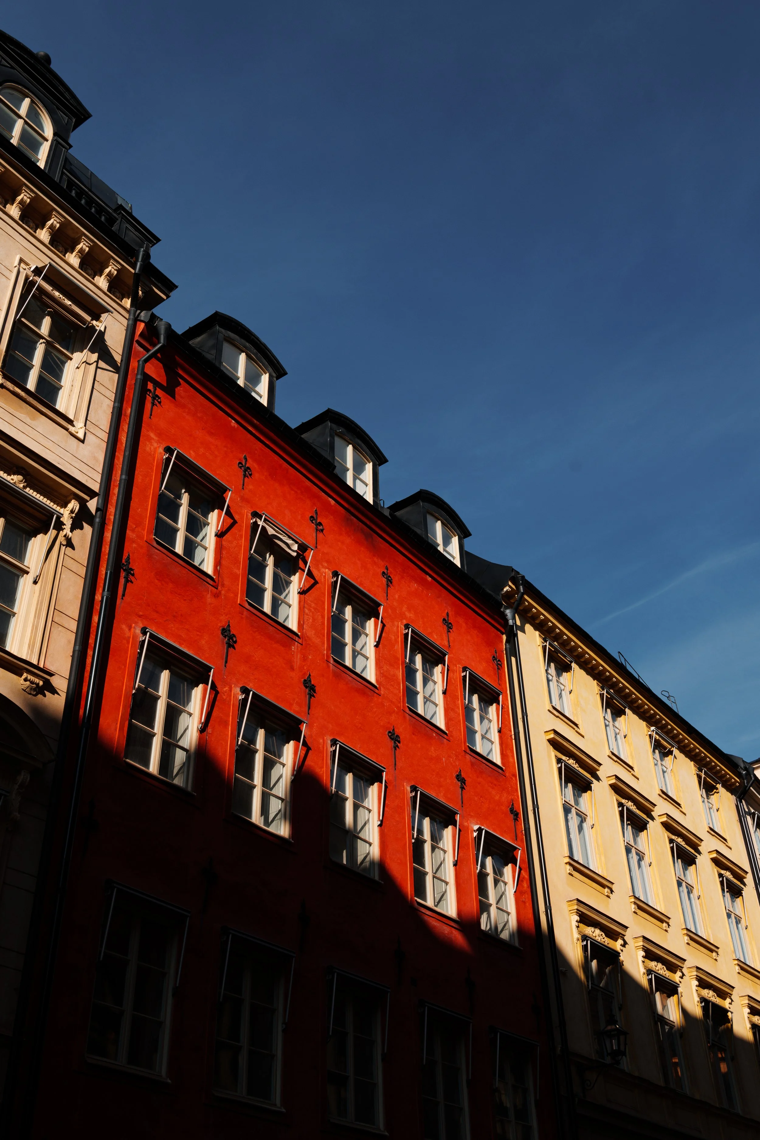 Colorful buildings in a city under a clear blue sky, with sunlight casting shadows on the facades.