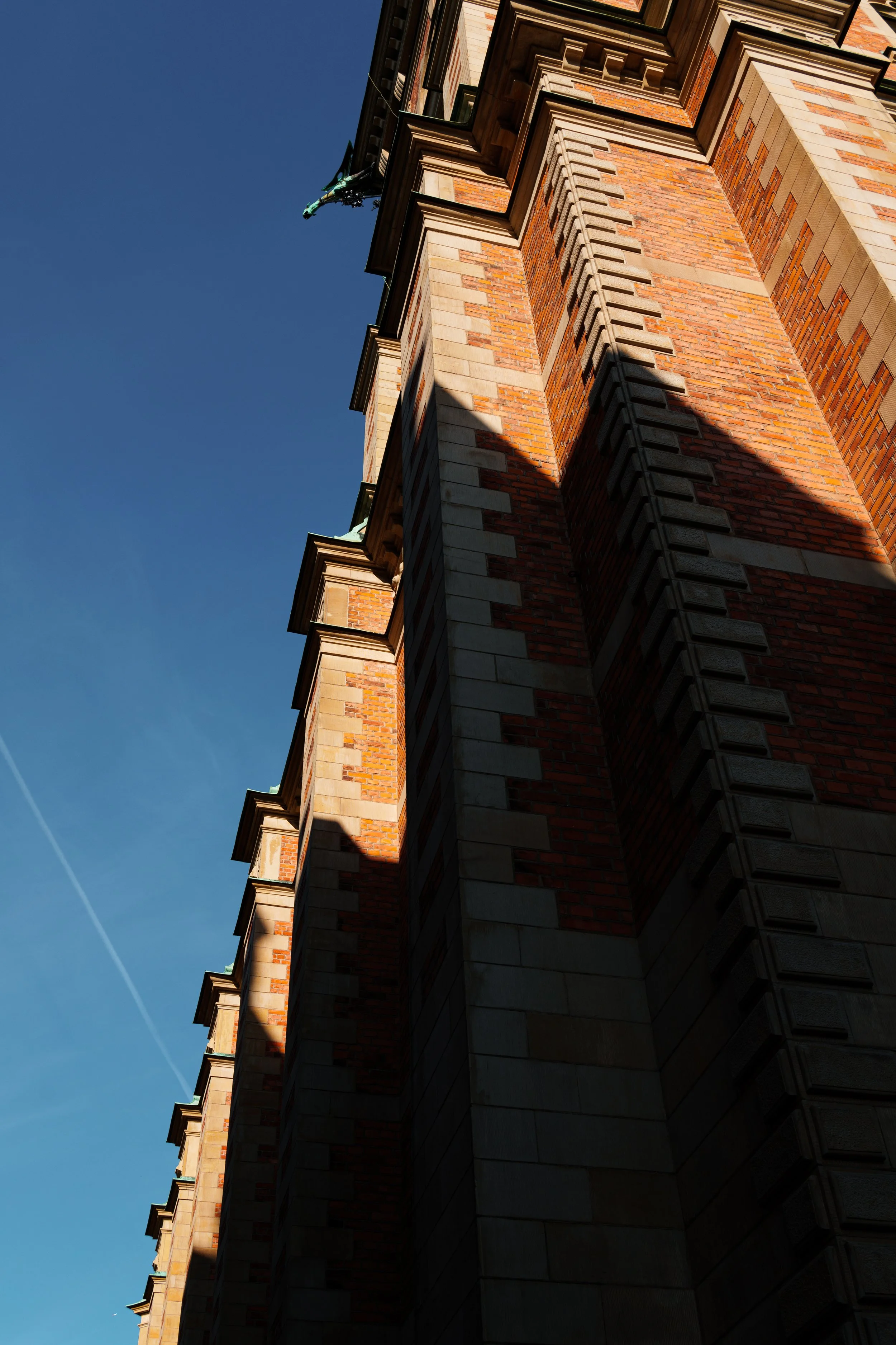 A tall brick and stone building seen from below, with shadows on its surface and a clear blue sky in the background.