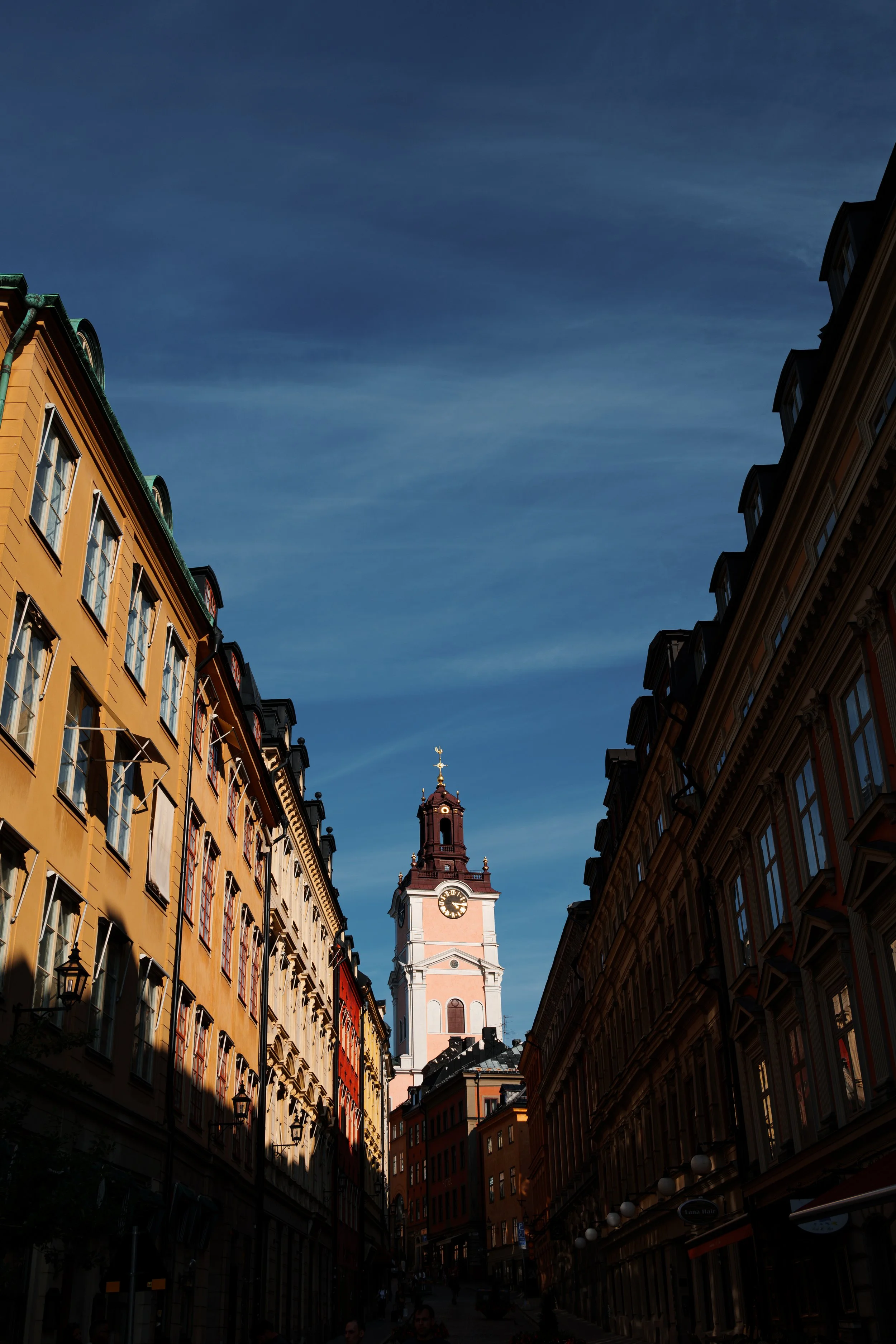 A street view of colorful buildings with a clock tower in the background under a blue sky.