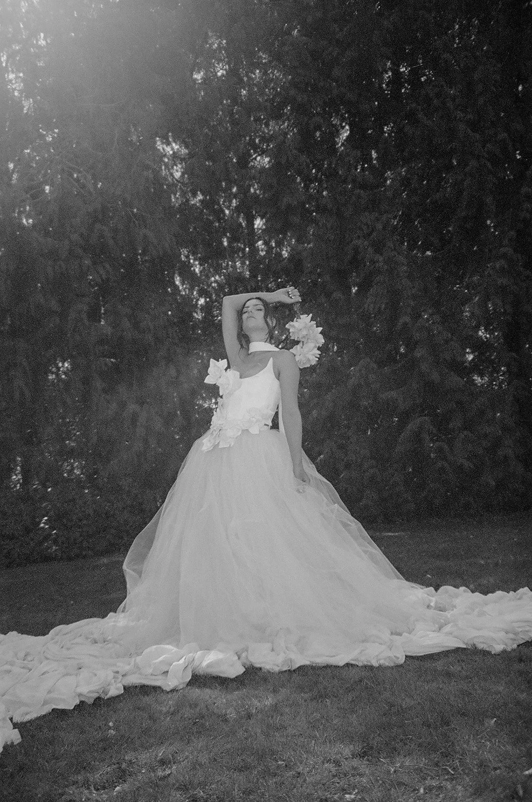 A woman in a wedding dress holding a bouquet of flowers, standing outdoors against a background of trees.