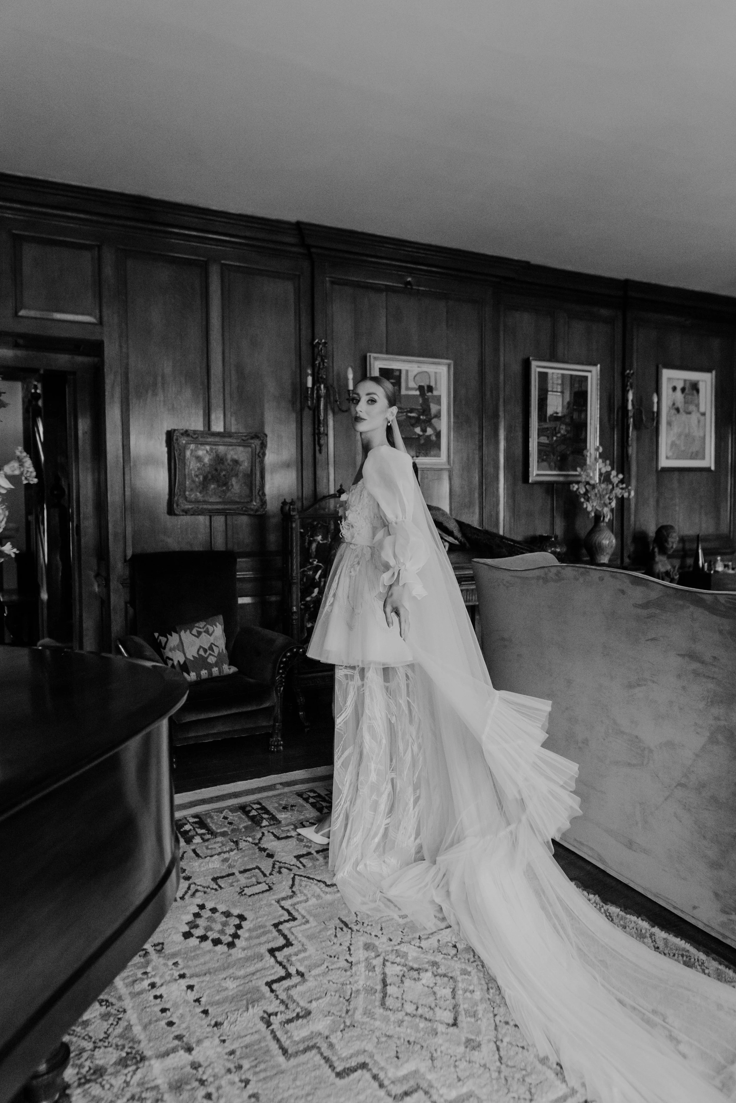 A woman in a wedding dress standing inside a room with wooden walls and framed artwork.