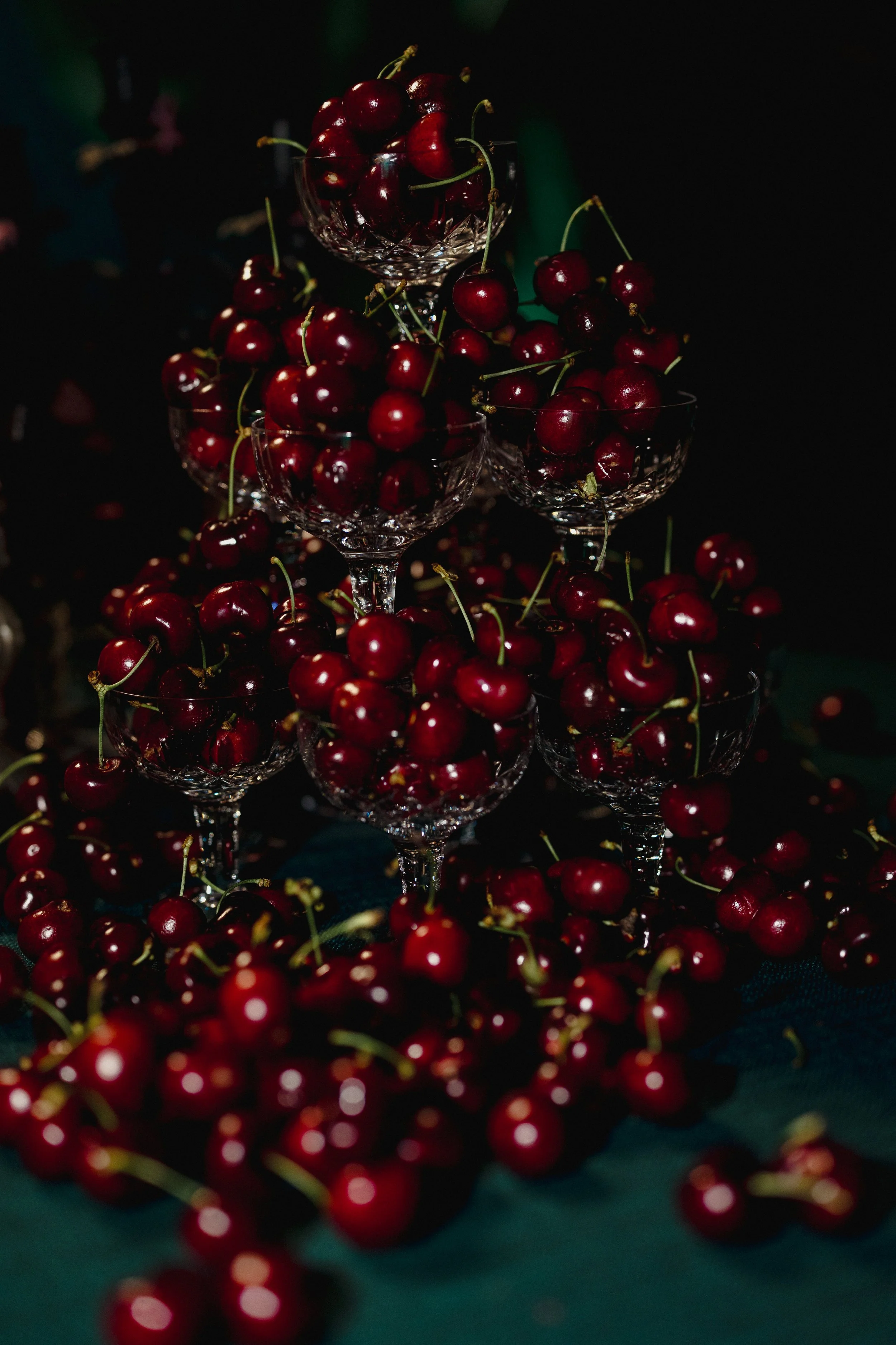 Several glass bowls filled with fresh cherries, some cherries are spilled around the bowls on a dark surface.