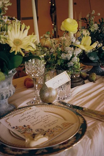 Table setting with floral centerpiece, crystal glassware, a place card, and decorative pears at a formal event.