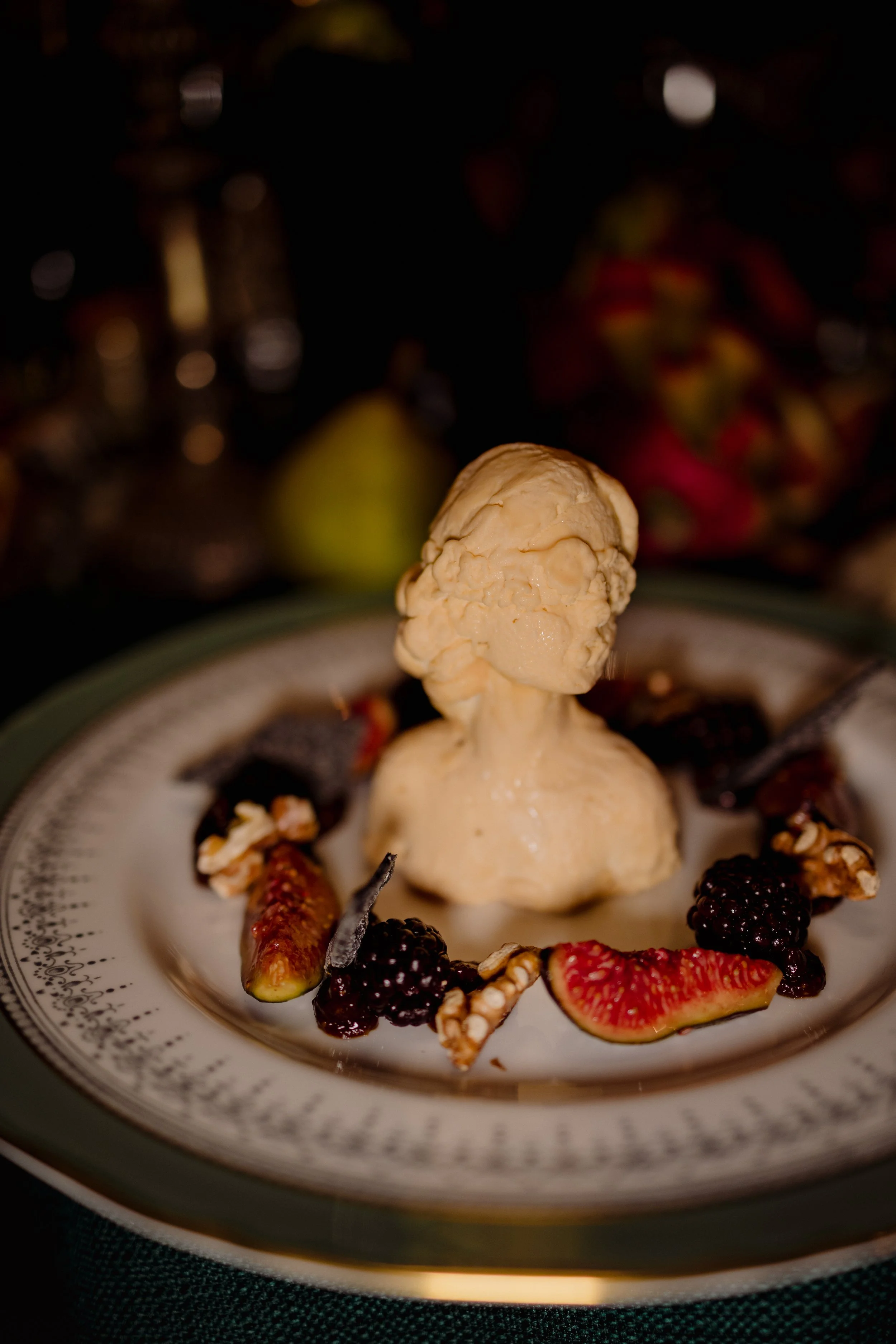 A scoop of vanilla ice cream shaped like a bust of a woman, garnished with blackberries, strawberries, and granola on a decorative plate.