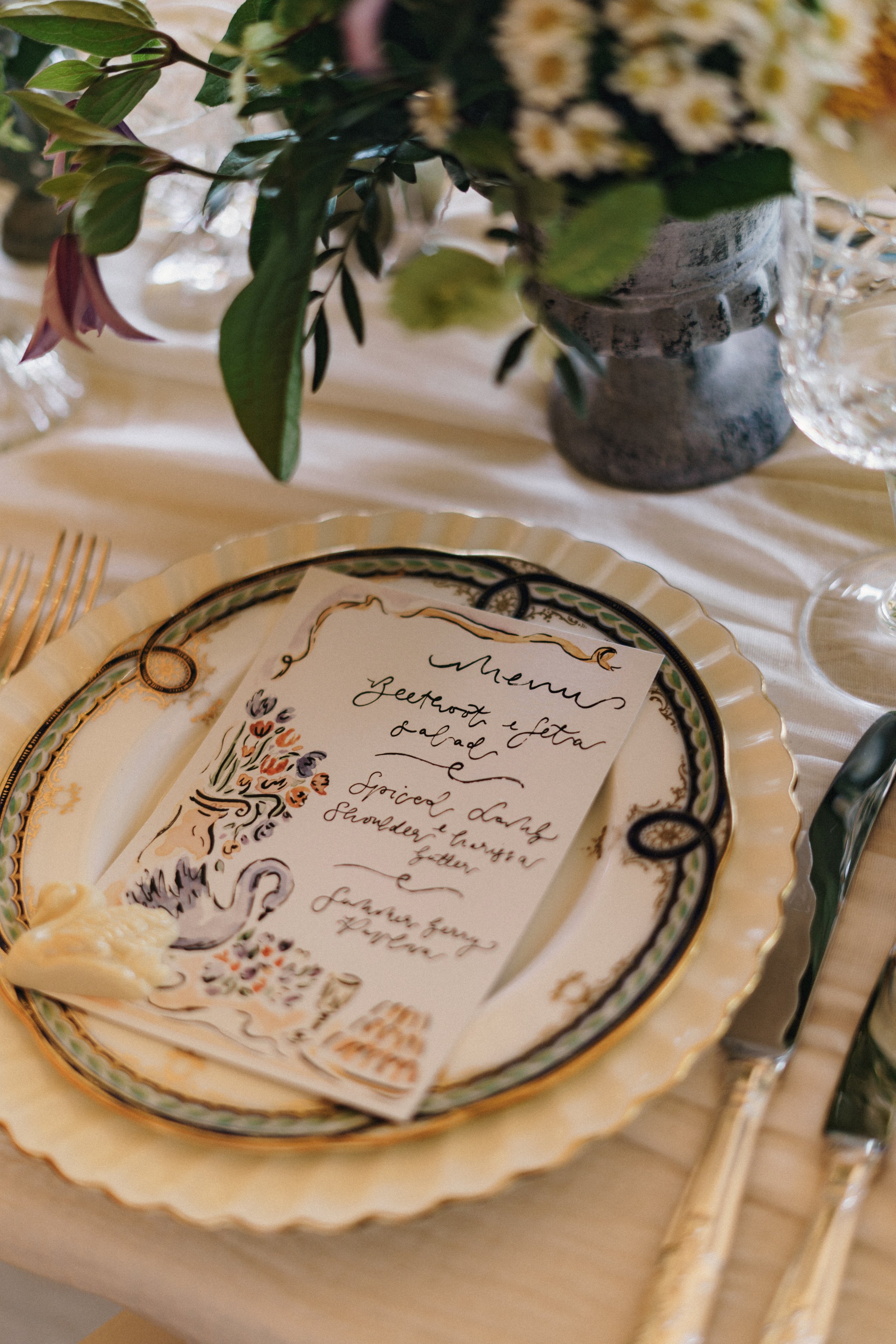 A decorated table setting with a plate, silverware, a floral centerpiece, and a handwritten menu card placed on a plate.